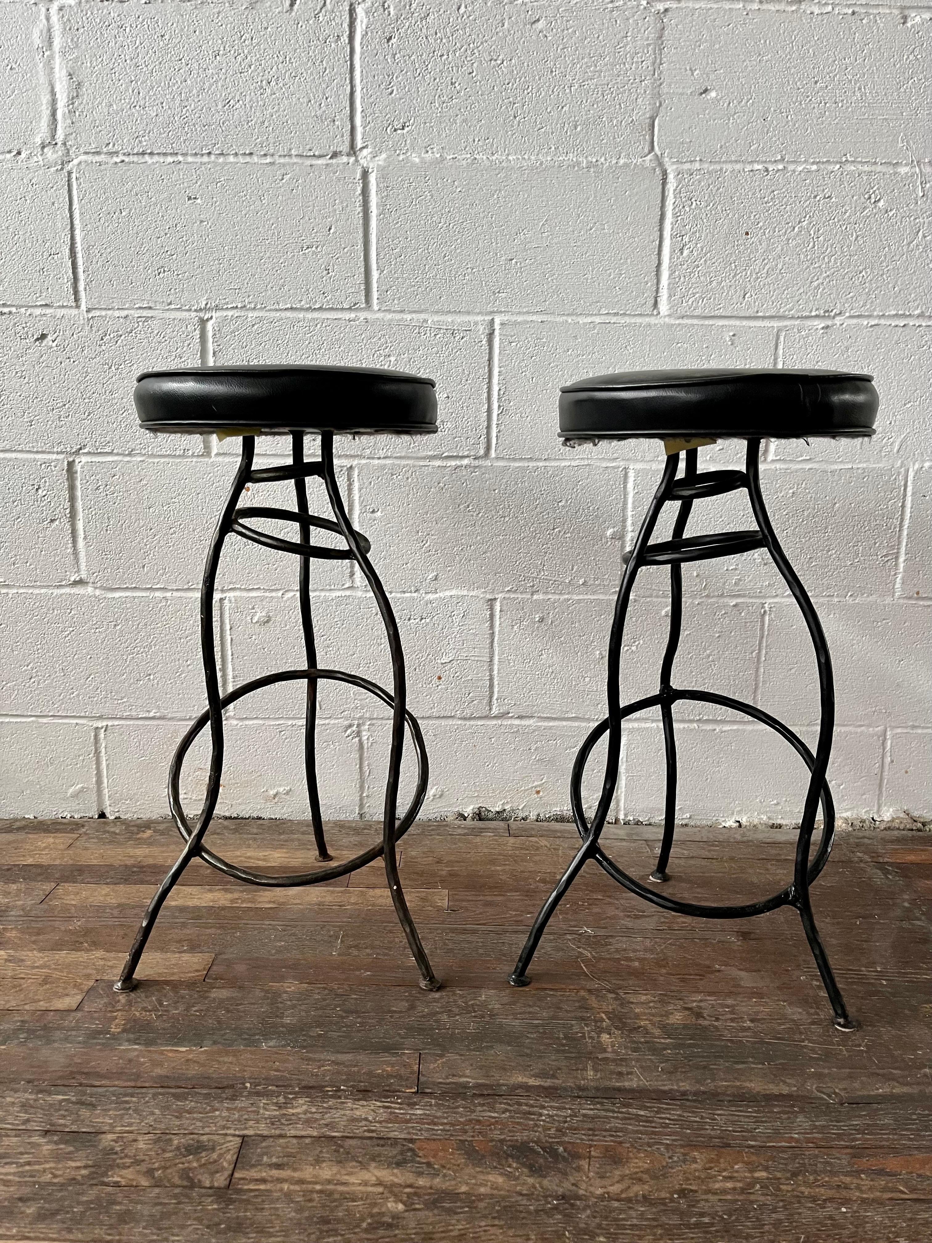 Einzigartiges Paar Barhocker aus gehämmertem Eisen mit schwarzen Vinylsitzen. Skurriles Design mit abgewinkelter Form. 
Bordsteinkante nach NYC/Philly $350