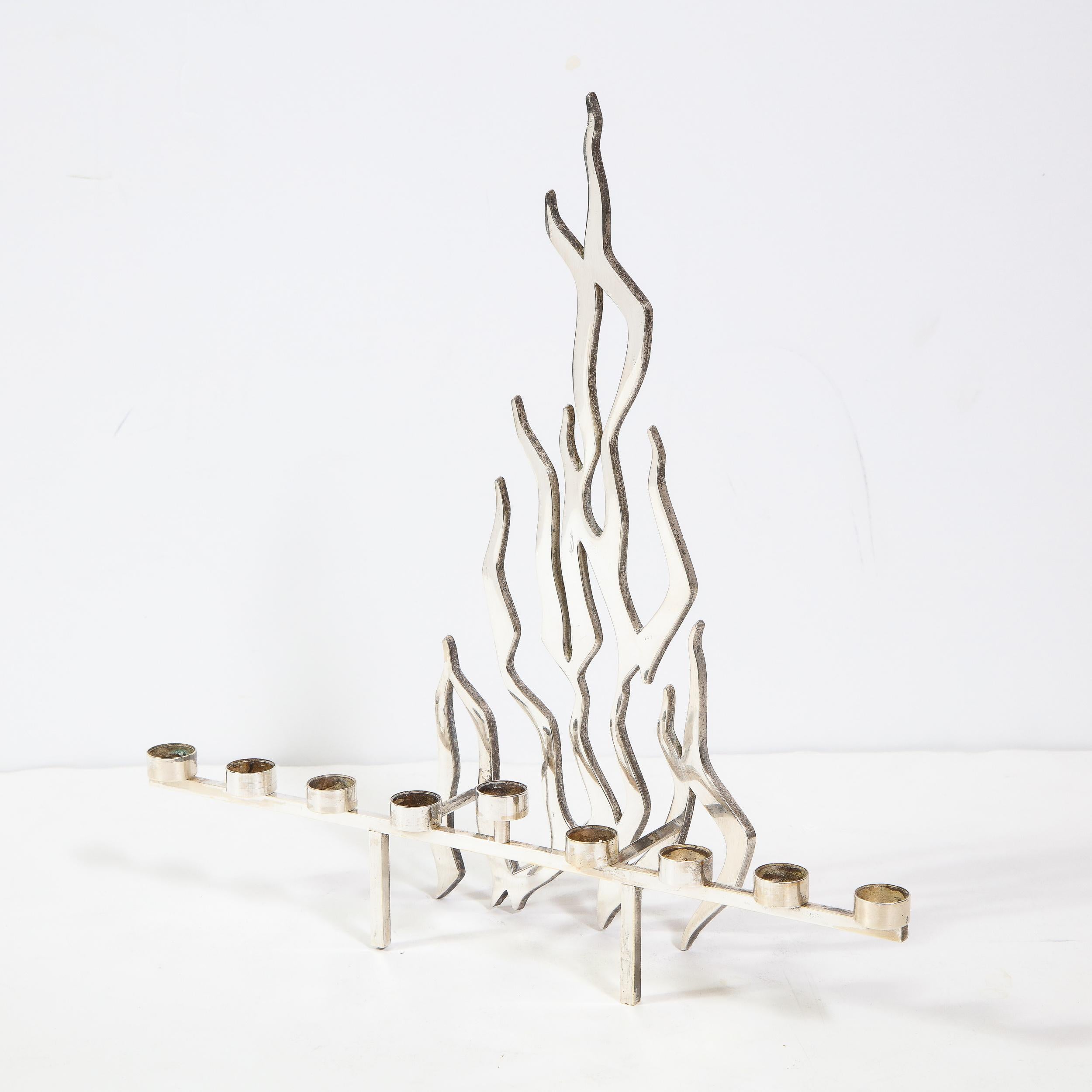 This stunning and graphic Mid-Century Modern Brutalist menorah was realized in Israel, circa 1960. Fabricated in silver plate, it features a candelabra stand composed of nine cylindrical candle holders (the center one appears raised via a