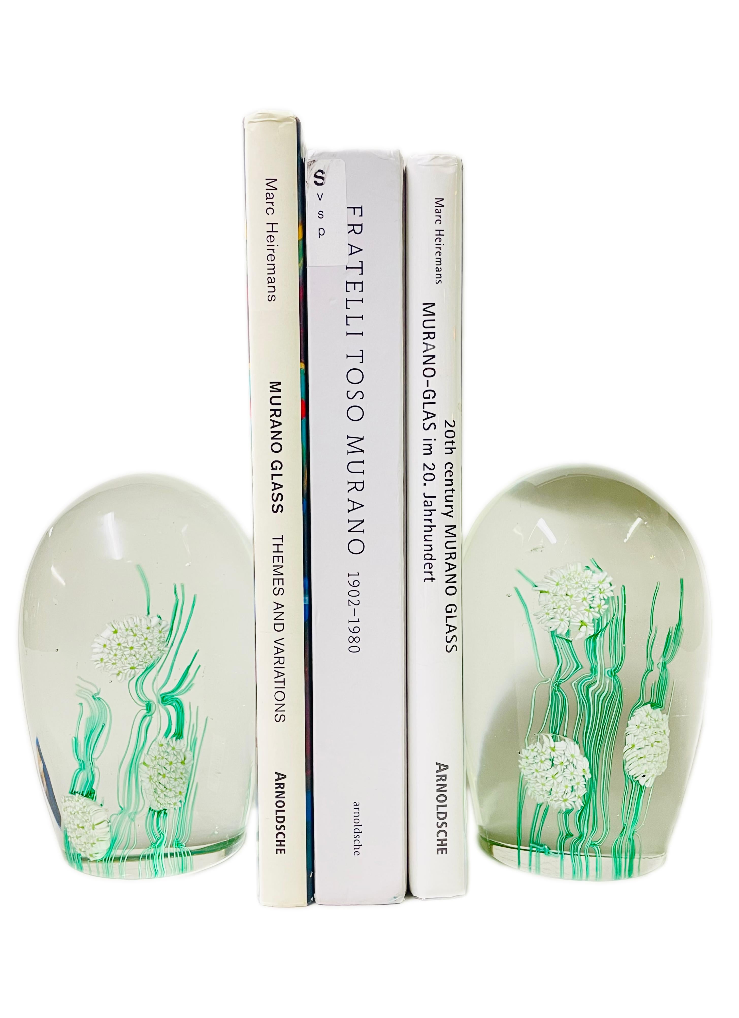 A Mid-Century Modern pair of Italian art glass bookends each decorated with Millefiori decoration of white flora and green leaf & vine cased in heavy clear glass in the form of bookends. The bookends are unsigned - circa 1970s - Murano, Italy