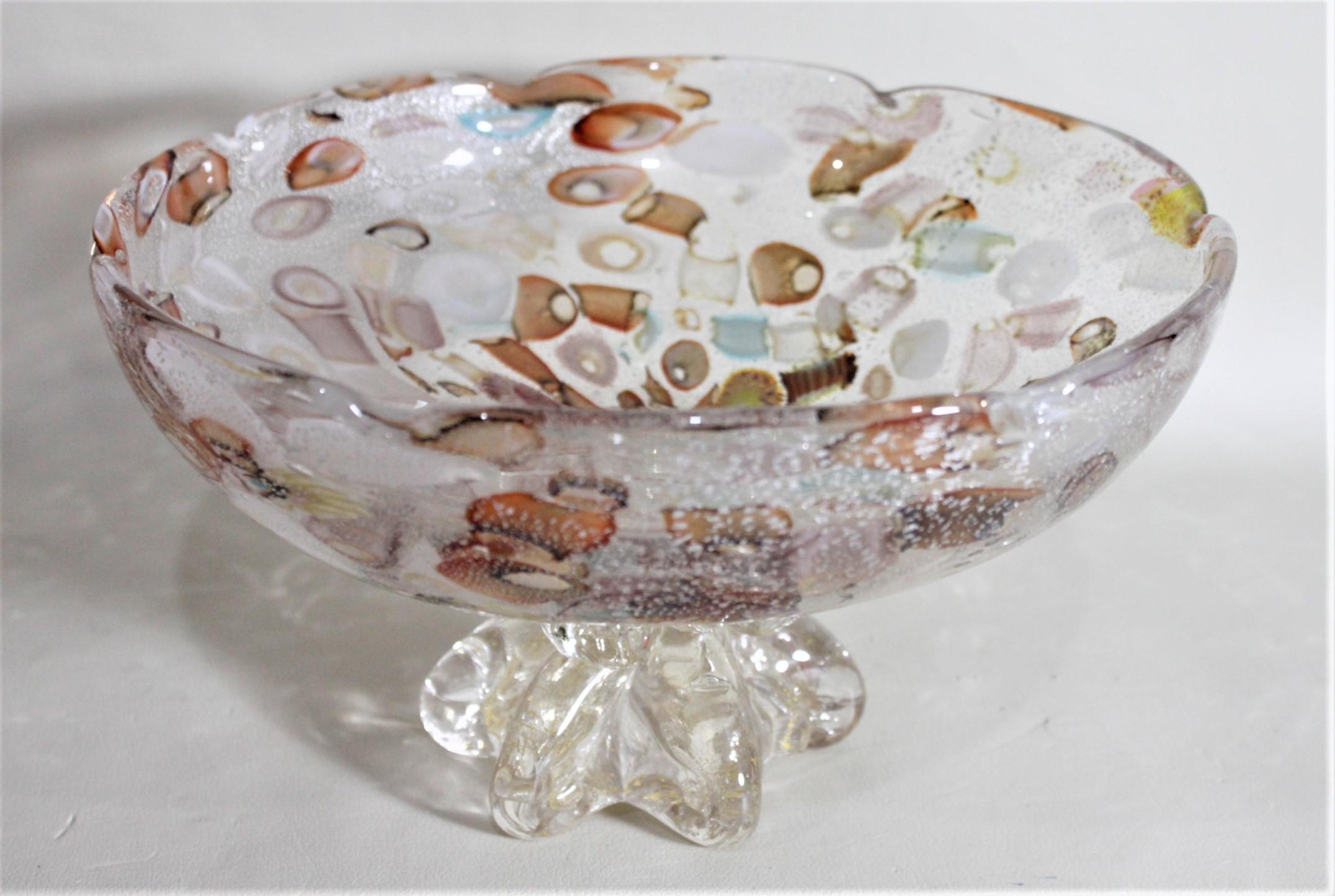 This large Mid-Century Modern art glass footed compote is unsigned but presumed to have been made in Italy in circa 1969. The bowl is done in multicolored swirls of red, brown, blue, white, yellow and orange on a clear background with silver flecked