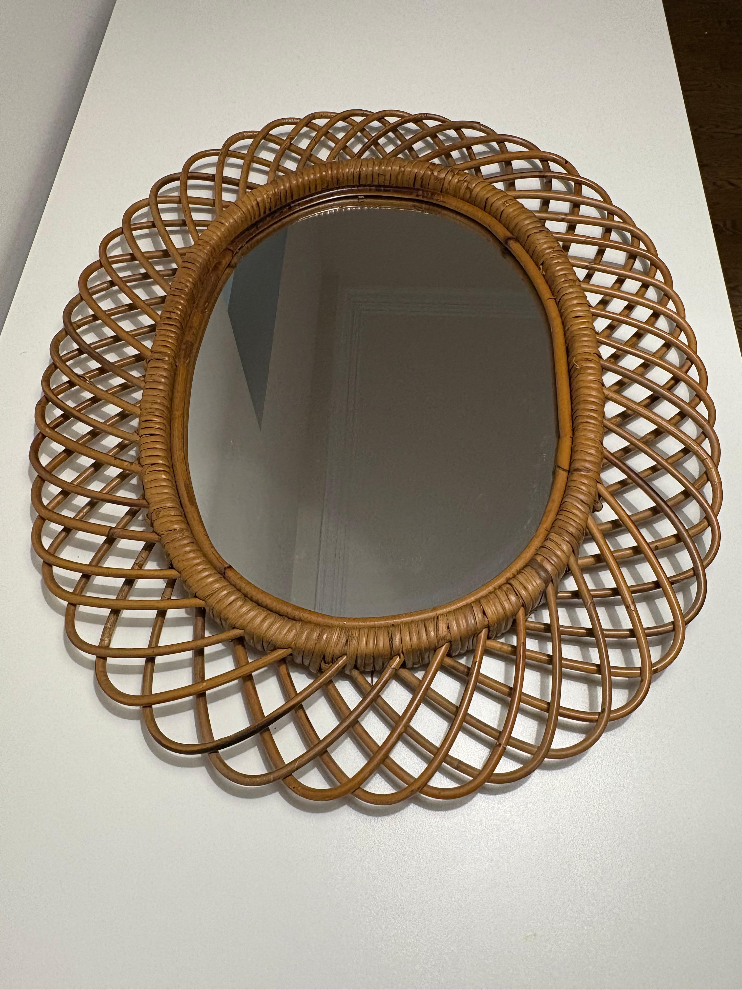 Magnifique miroir ovale en bambou et rotin. Ce miroir de style italien Franco Albini présente des boucles de bambou maintenues dans des bandes de rotin autour du grand miroir. Ces miroirs artisanaux étaient typiques de l'Italie des années 1950 aux