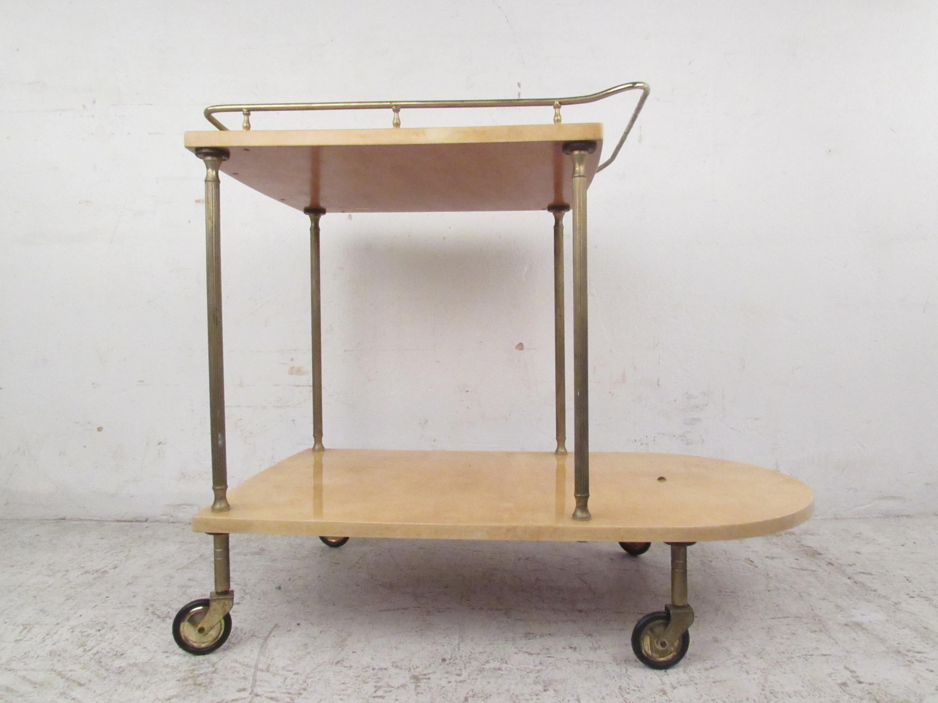 This stunning vintage modern bar cart boasts a gorgeous cream colored goatskin and brass fixtures. The elegant lacquered goatskin and decorative supports add to the midcentury appeal. This sleek two tier serving cart makes the perfect addition to