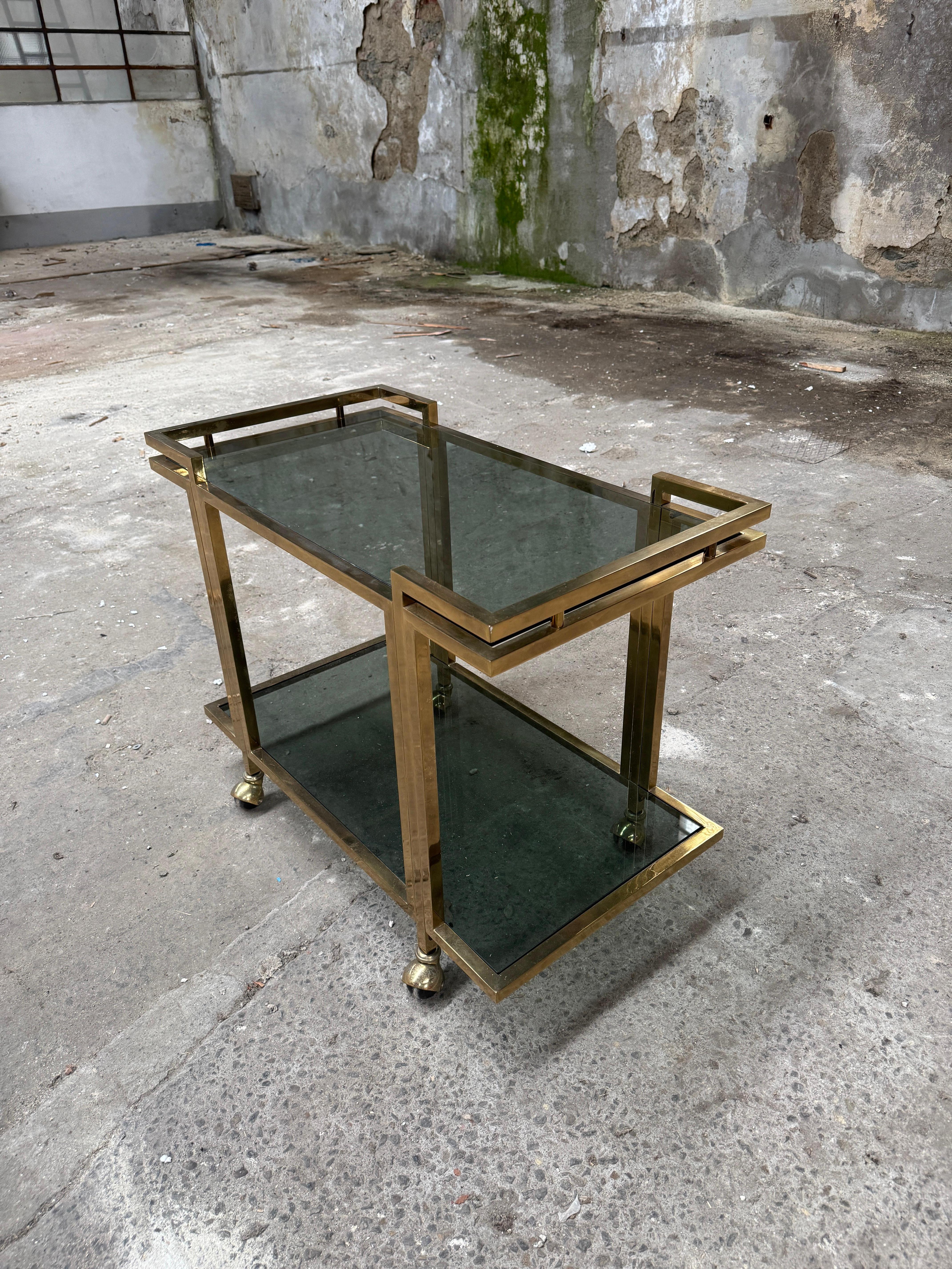 Entrez dans l'élégance intemporelle des années 1970 avec ce chariot de bar en laiton exquis, une véritable pièce d'apparat pour tout intérieur sophistiqué. Fabriqué avec un cadre en laiton géométrique et élégant, ce chariot vintage exsude le charme