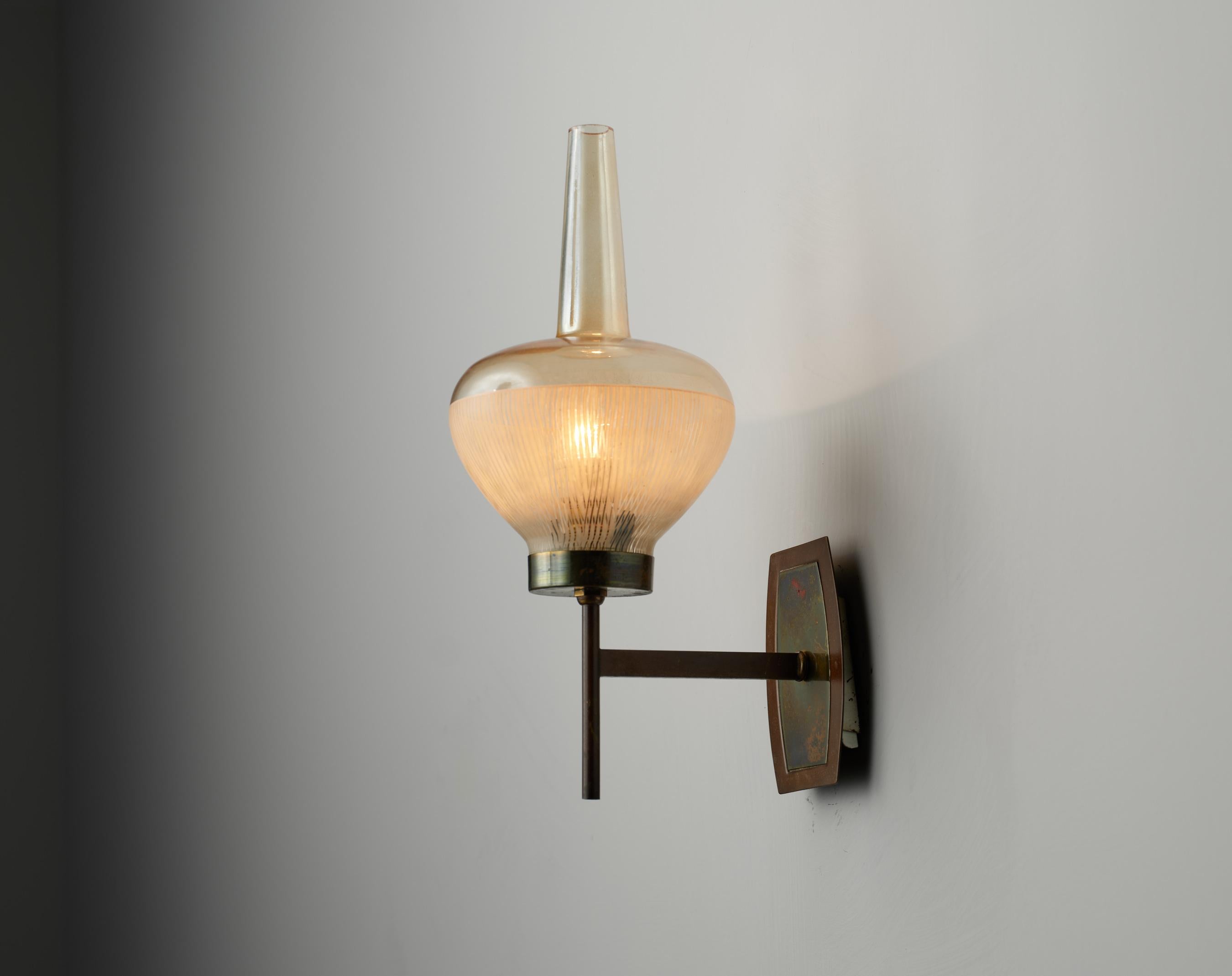 This wall-mounted sconce exemplifies the refined aesthetics of mid-century Italian design. Crafted in the 1960s, the fixture features a durable brass arm that extends from a rectangular wall plate, presenting a spherically shaped shade made from