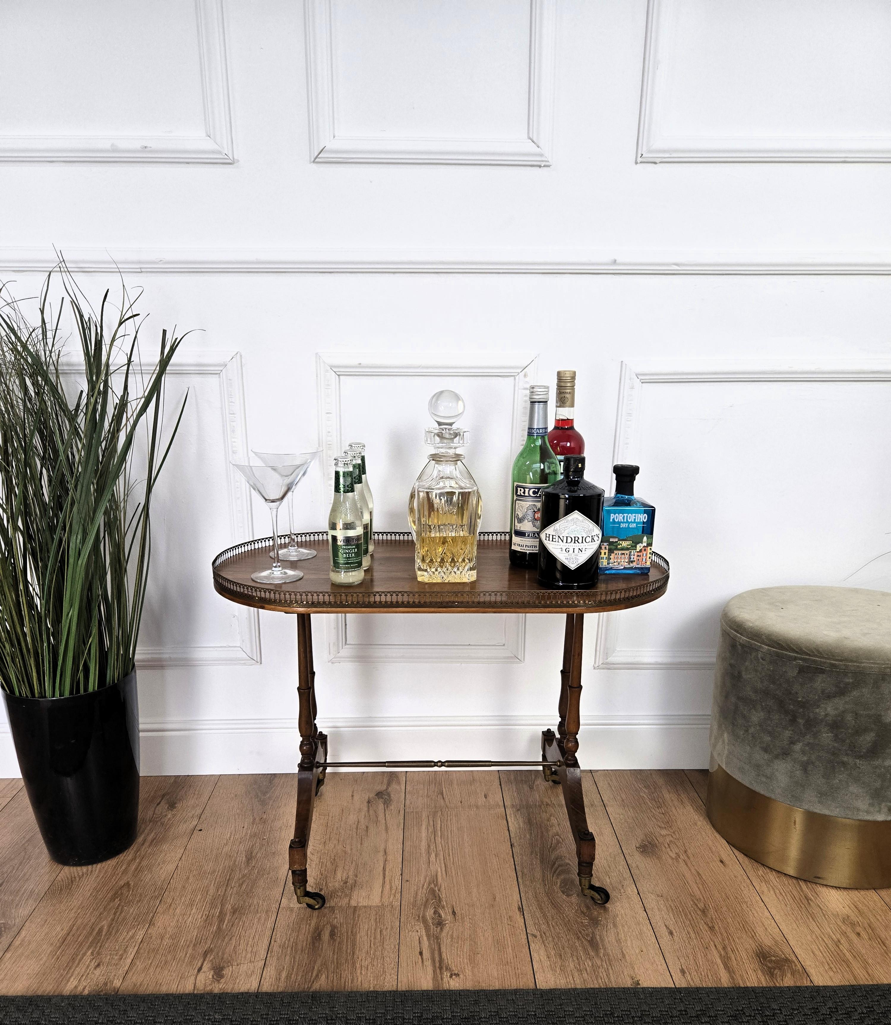 Un bellissimo tavolino in noce italiano con grandi dettagli e cornici, di forma ovale con una bella struttura in ottone e gambe intagliate con barella centrale in ottone completata da ruote in ottone. Un pezzo molto elegante, moderno e classico che