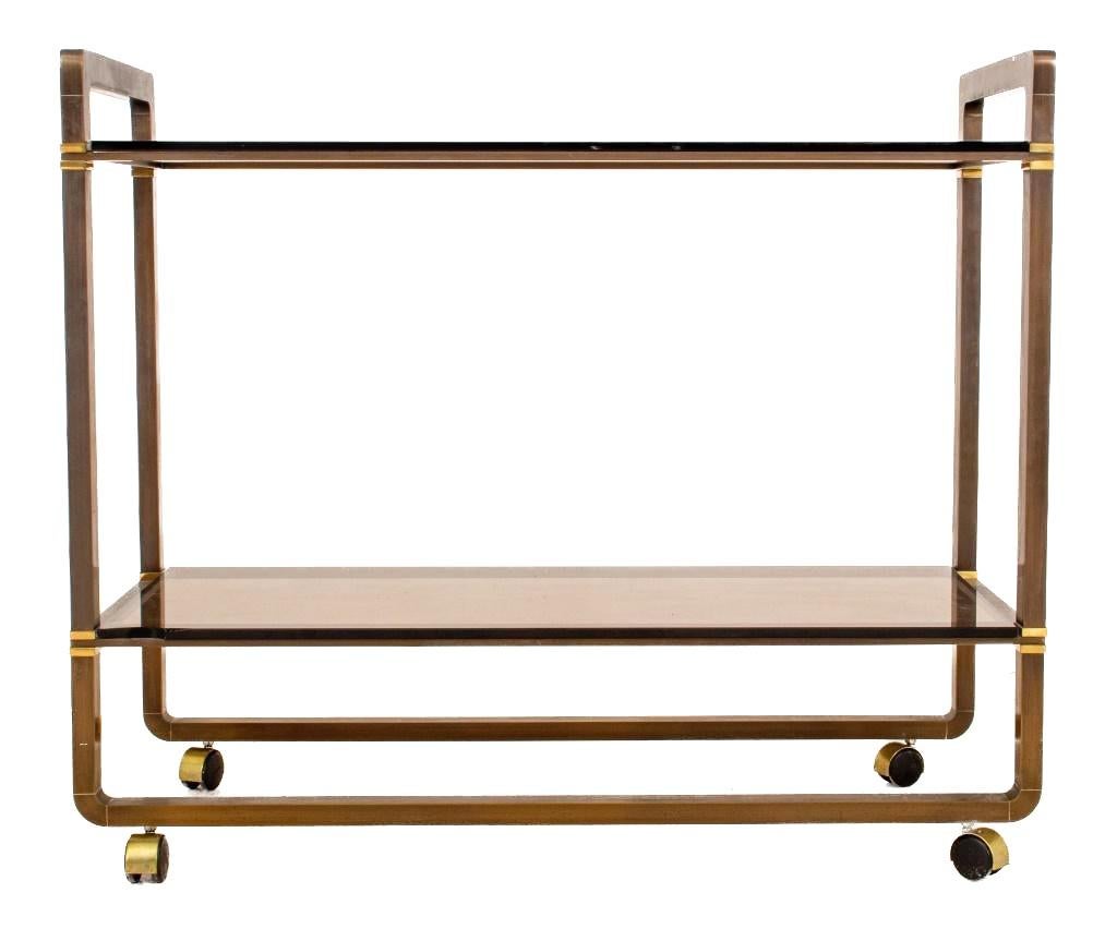 Beautifully made in the Mid-Century Modern style two tiered glass shelving serving cart. The cart features two tinted glass shelves with two holding side handles resting on four wheeled. This vintage bronze and gilt brass serving cart also features