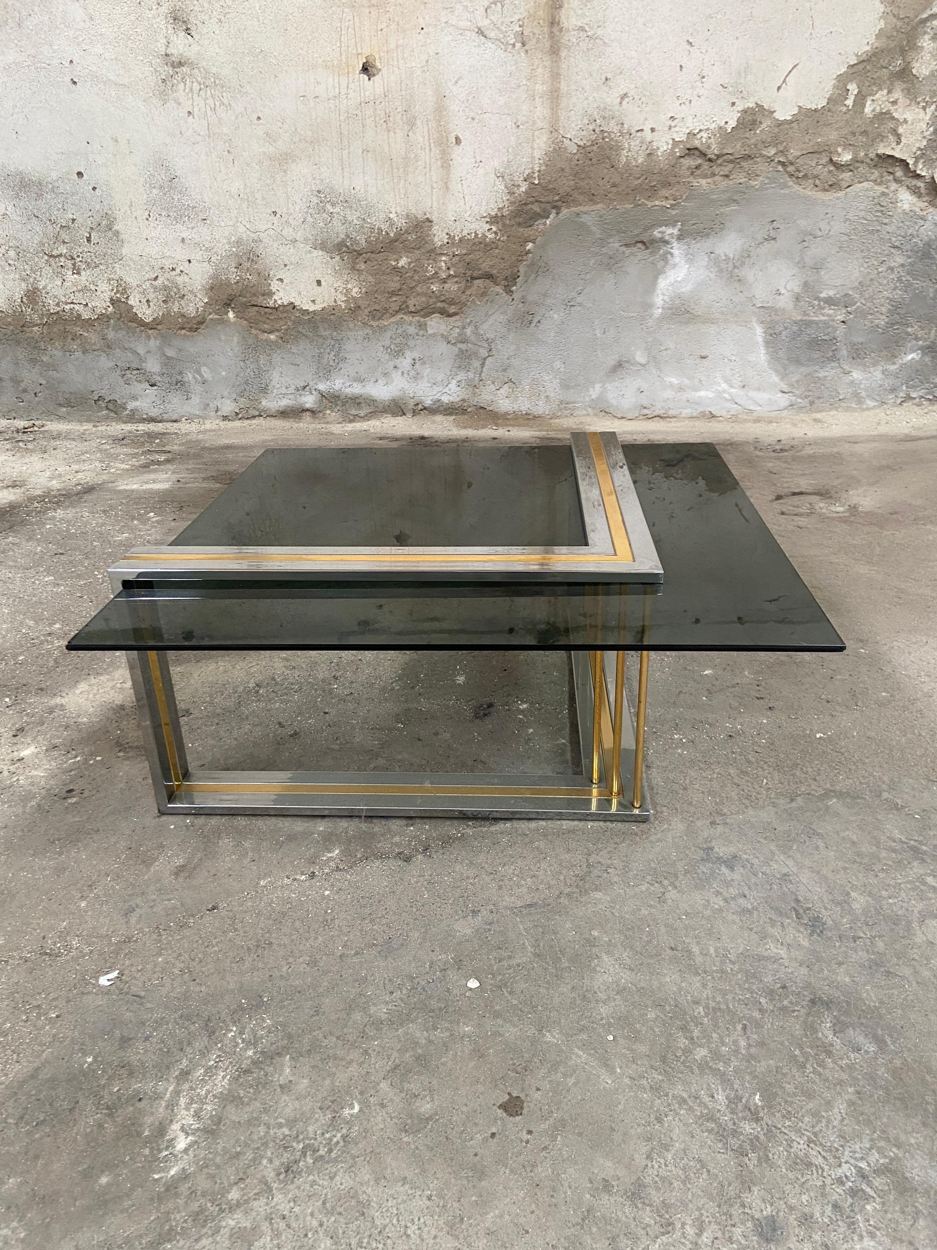 Mesa de café o sofá italiana de mediados de siglo de Romeo Rega. La mesa tiene una estructura de cromo y latón y un tablero de cristal ahumado.
Un par de bordes del cristal tienen pequeños desconchones por debajo, pero en conjunto la mesa está en