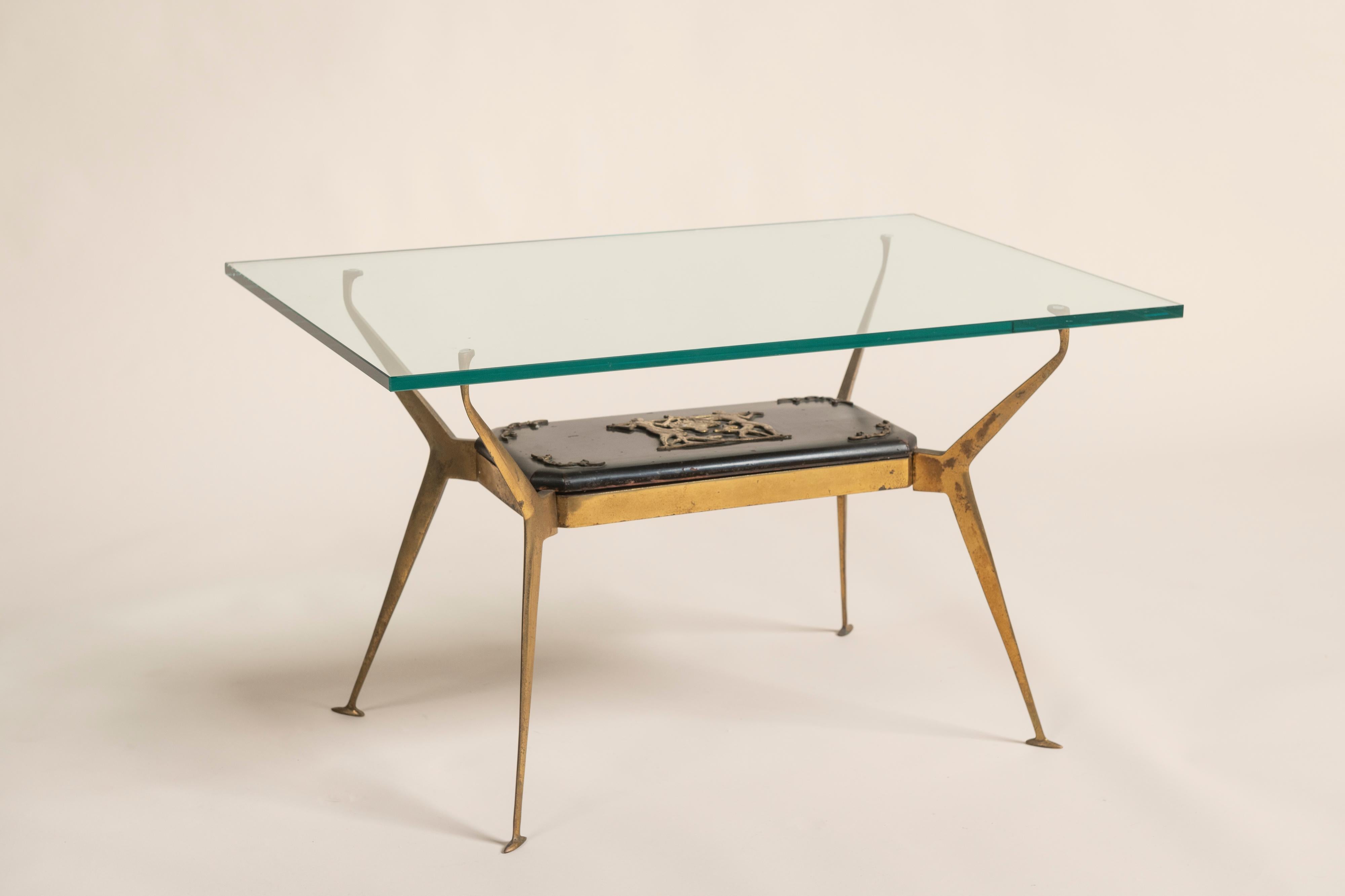 Charmanter Couchtisch mit massivem Messingfuß, unterer Ablage aus Holz mit Bronzeverzierung und Glasplatte. Die Ornamente zeigen eine Frau und einen Mann, die einen Blumenkorb tragen, begleitet von springenden Hunden. Hergestellt in Italien in den