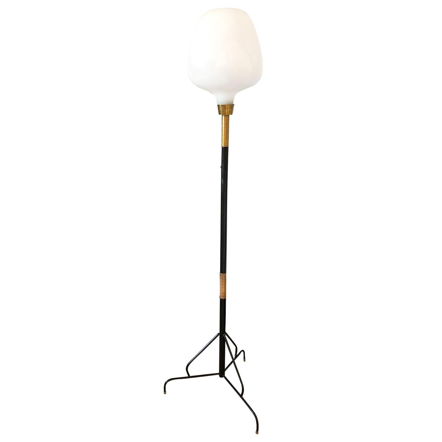 A vintage Mid-Century Modern Italian floor lamp made of hand crafted lacquered metal and brass with one frosted opal glass shade, featuring a one light socket, standing on three slightly curved metal legs, in good condition. The shade is slightly