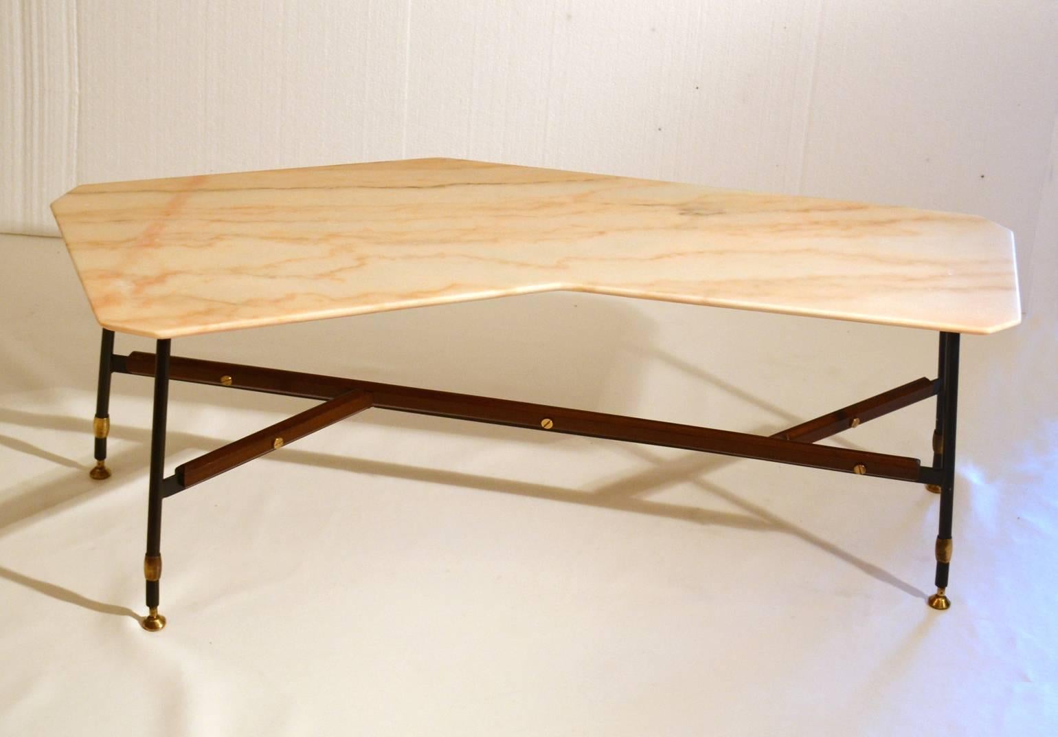 Marble coffee table, off-white with peach color veins, is cut in free form geometrical shape. The black metal frame has strips of mahogany attached and stands on brass feet. The table is versatile in use; perfect as a center table but due to its
