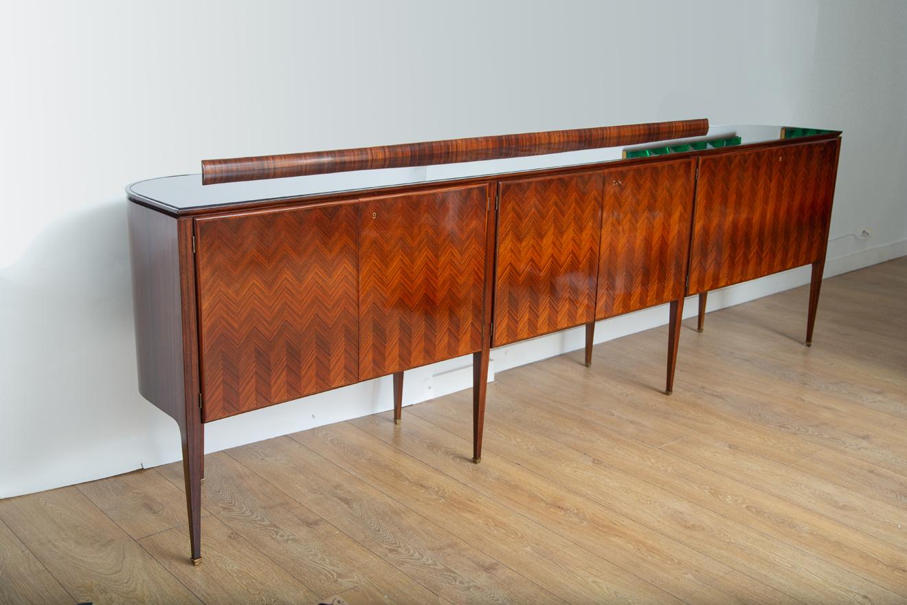 Rare Italian mid-century modern large and narrow sideboard by Paolo Buffa. 
 Graciously curved Indian rosewood encasement with chevron pattern
 Tapered legs with bronze sabots.
 Burgundy inset glass top.
Three double doors concealing maple