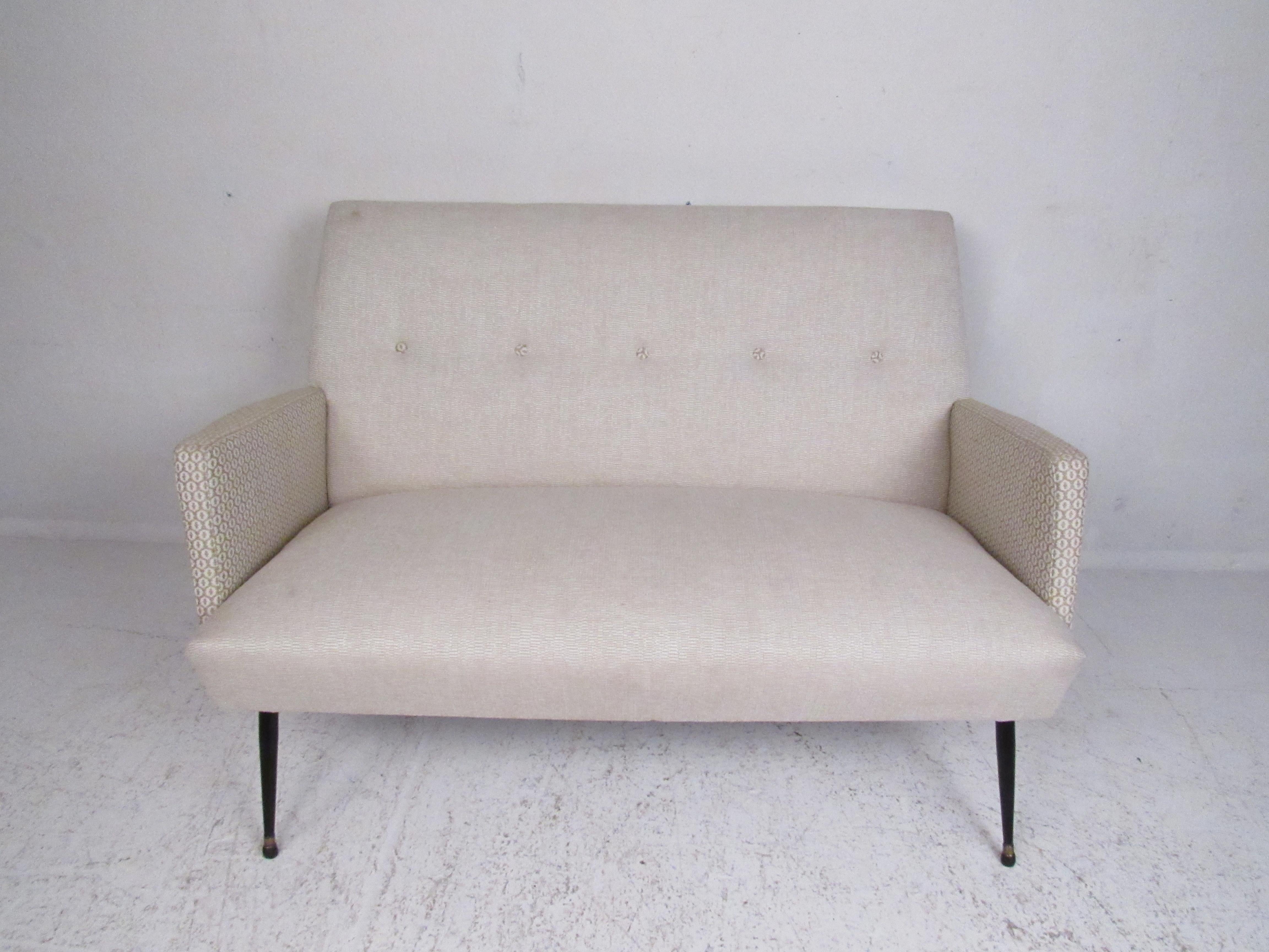 Dieses atemberaubende italienische Sofa im modernen Vintage-Stil verfügt über gespreizte Metallbeine mit Messingfüßen und eine getuftete Rückenlehne. Ein bequemes Sofa mit cremefarbener Polsterung und dekorativen Armlehnen. Dieses stilvolle Sofa ist