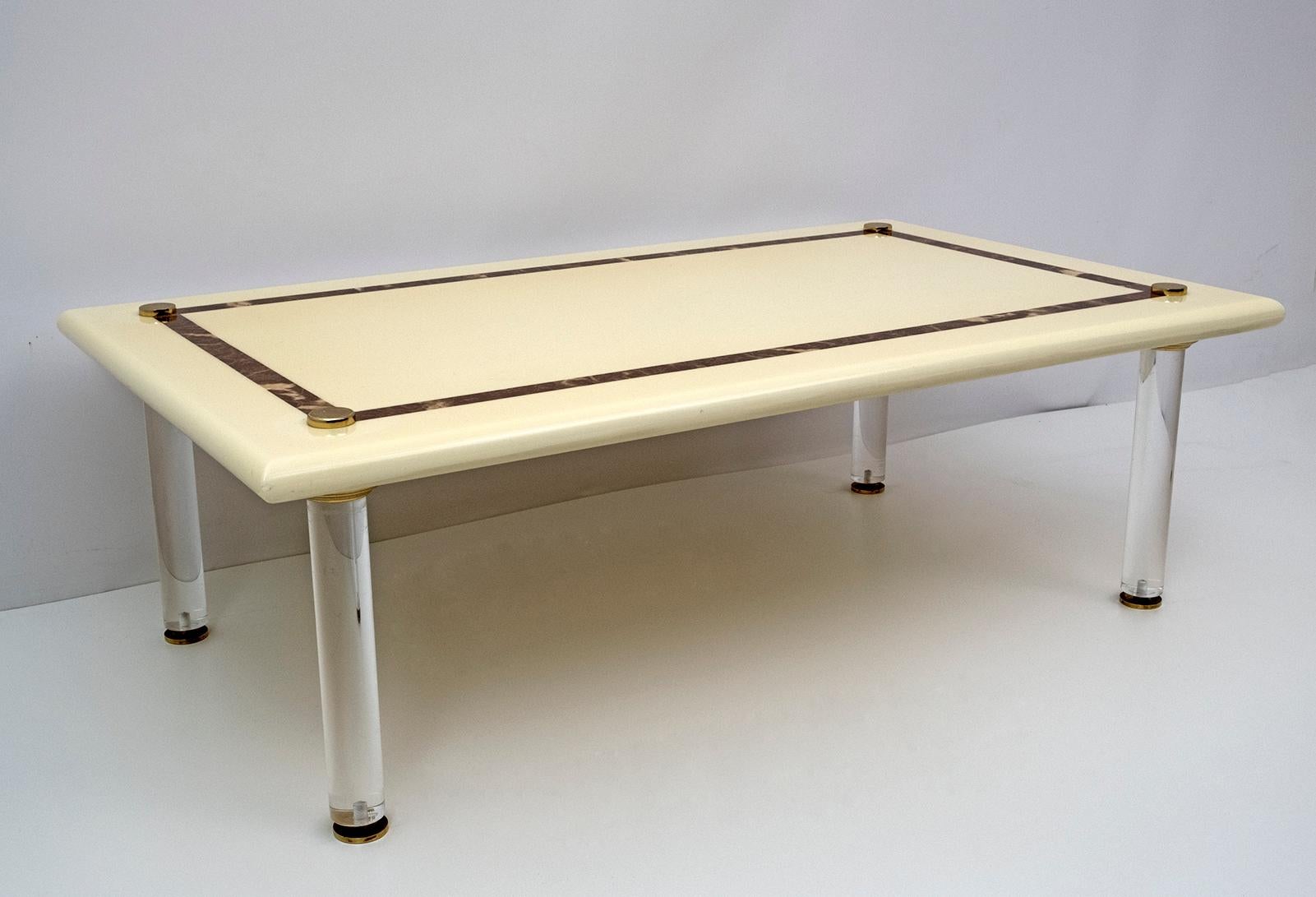 This coffee table has an ivory lacquered wooden top with a marble effect motif and feet in lucite and brass, production of the 70s.