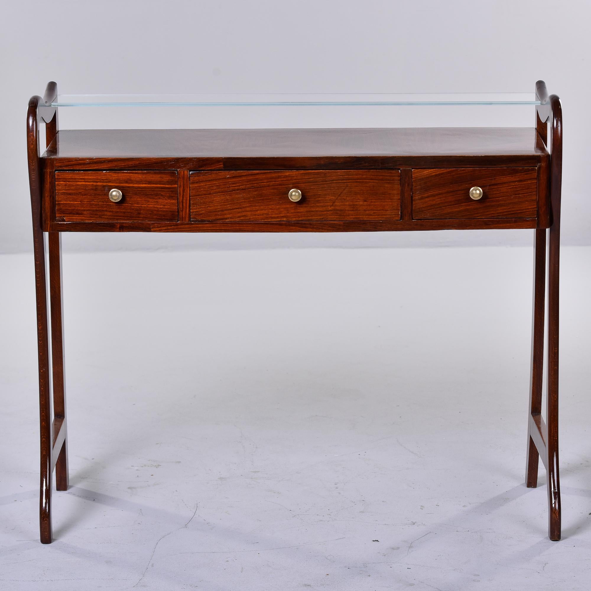 Found in Italy, this circa 1960s mahogany console is just under 40” wide. Console’s top level has a glass shelf that is half the depth of the console with three functional drawers below. Unknown maker. Versatile size. Very good vintage condition.