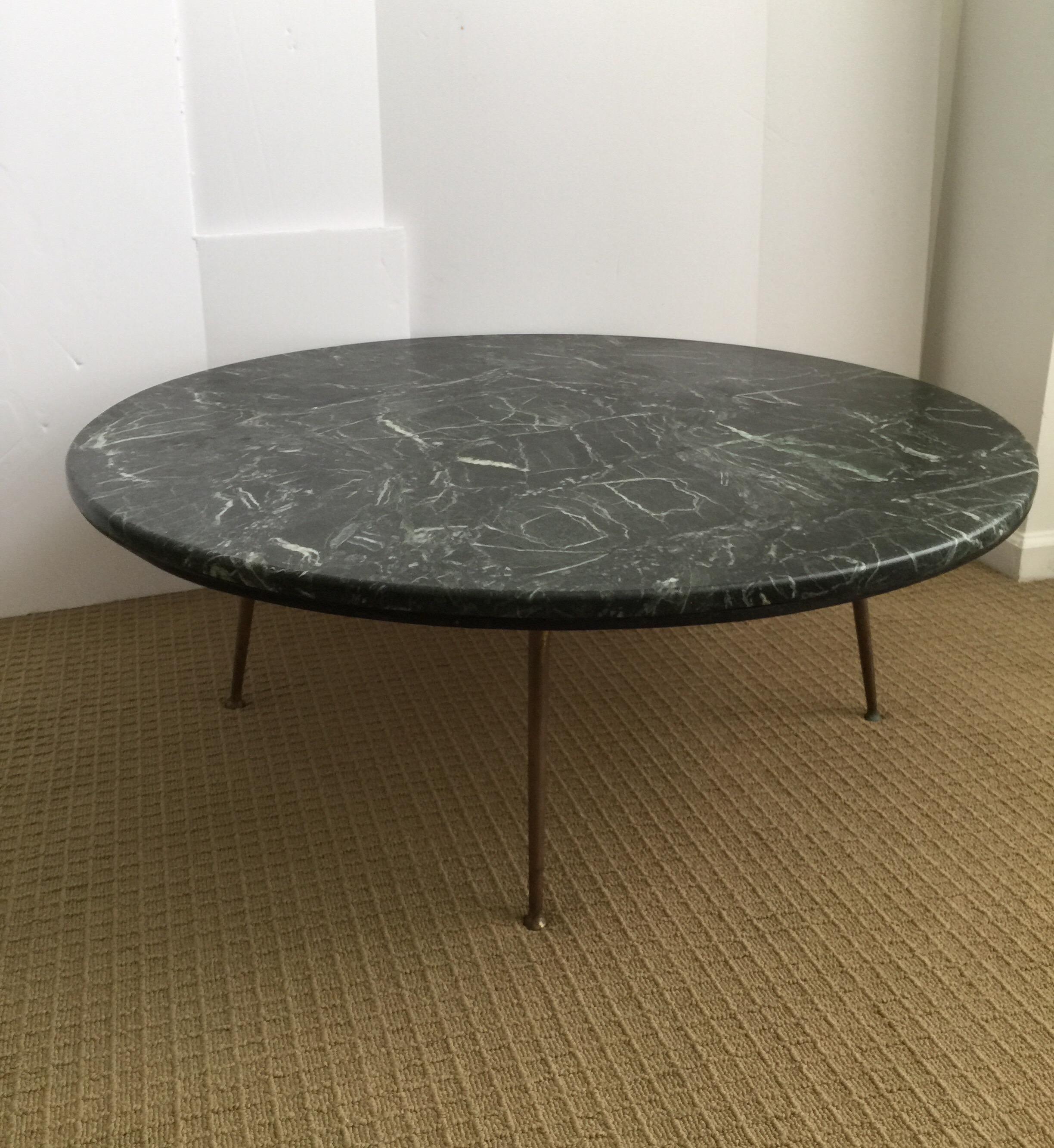 Large round Mid-Century Modern marble coffee table with brass or bronze metal legs. This sleek cocktail table features a marble top with black, white, and deep green tones. Marble sits on top of a wood base and is removable. Minimalist atomic era