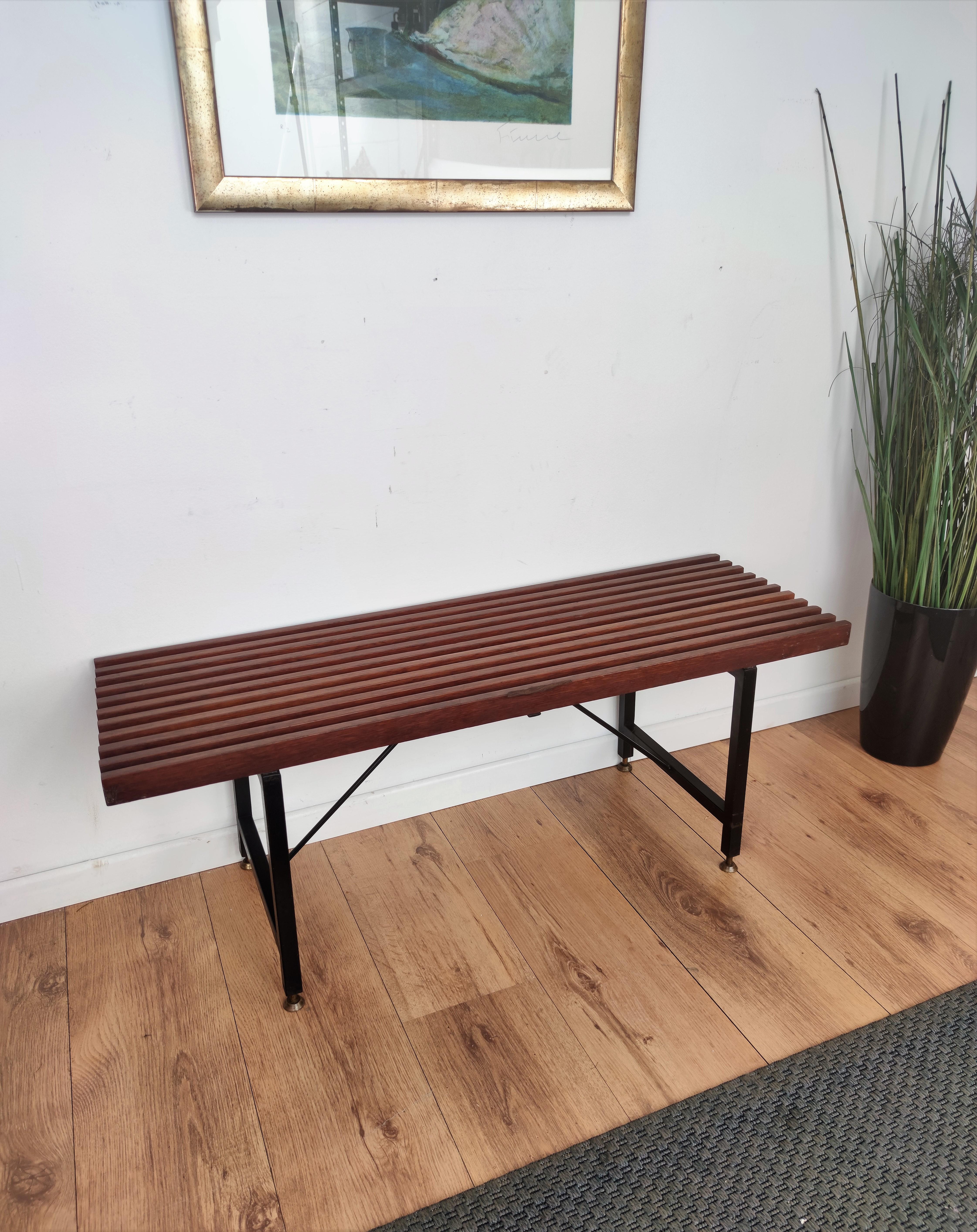 Italian Mid-Century Modern platform slat bench with wood slated top sitting on black metal cross bar base and nice brass foot-ends. The perfect piece for a house or building with large expansive windows or a long entrance way for seating or can be