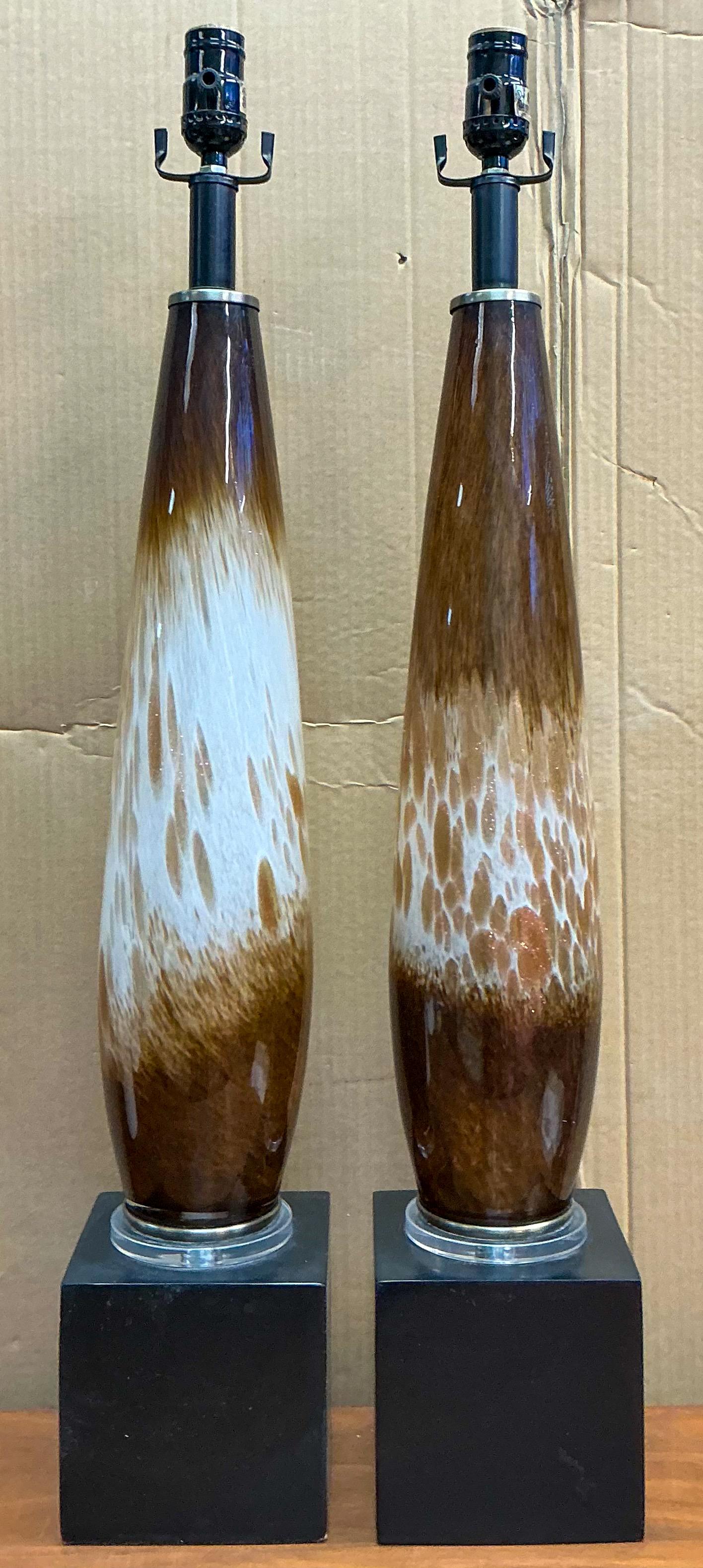 This is a pair of mid-century modern Italian hand blown glass table lamps by Murano. The cylinder glass flows white to brown with gold flecks through the body. They are mounted to black square bases. The sockets were re-done in 2012.