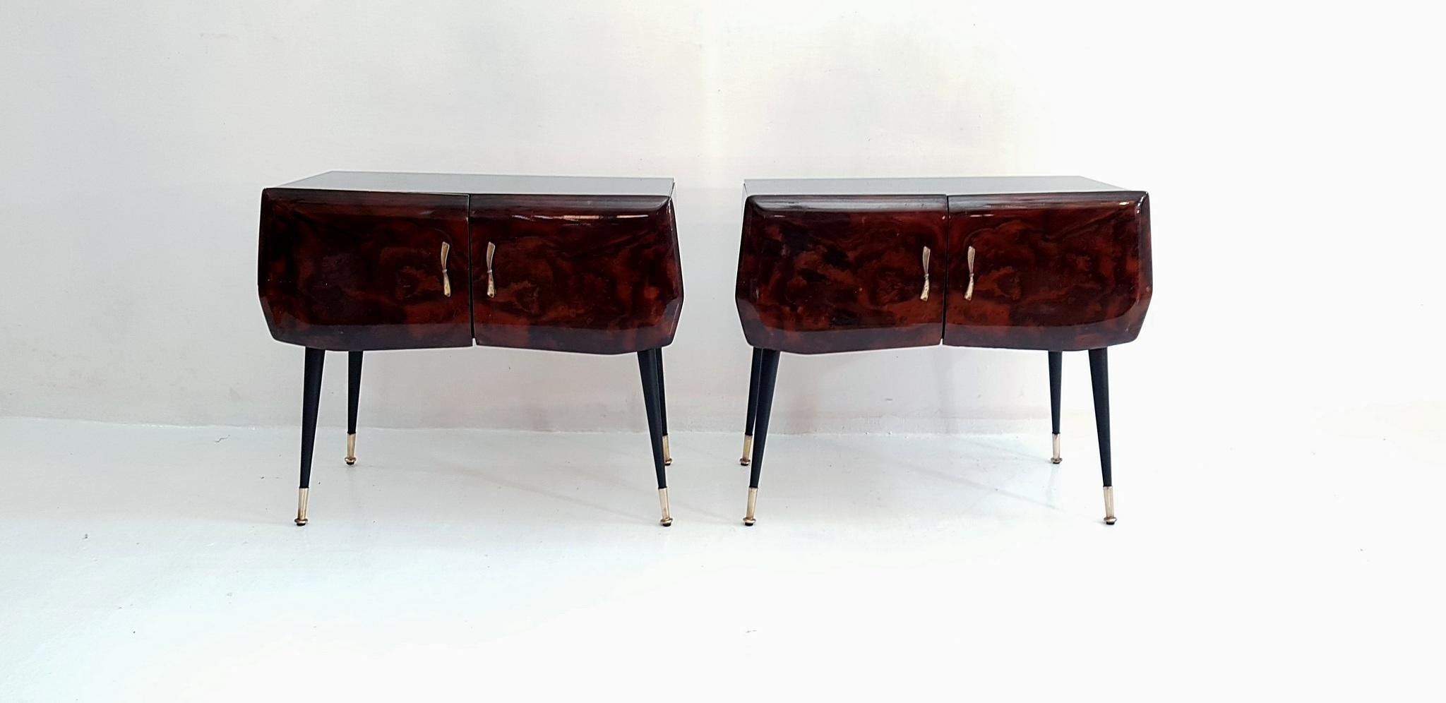 A pair of beautiful Italian nightstands resting on spider legs in iron and brass with double doors, each with handles in brass made to look like bows. They have a black glass top and the front of the doors has veneer from maple root. The inside are