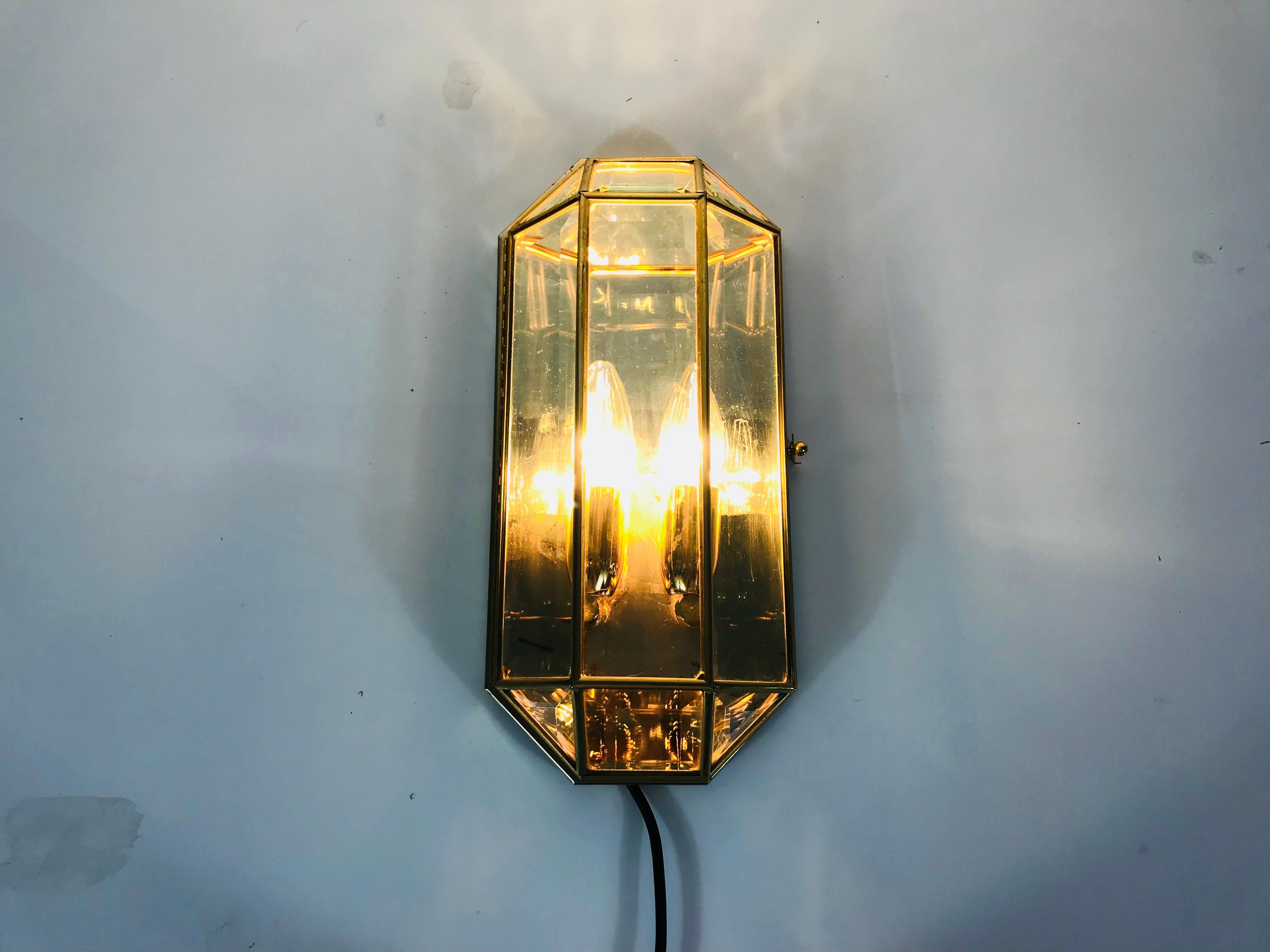 A midcentury wall lamp made in Italy in the 1960s. The lamp shade has an octagonal shape and is made of glass and golden metal. The back is aluminium.

The light has two sockets which require an E14 light bulb.