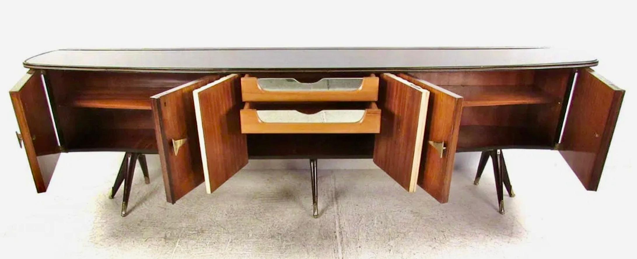 This stunning oversized Italian sideboard features rosewood finish cabinet doors mixed with unique lacquer and brass details. Formica style top adds durability and style, while tapered brass tipped legs enhance the Mid-Century appeal of the piece.