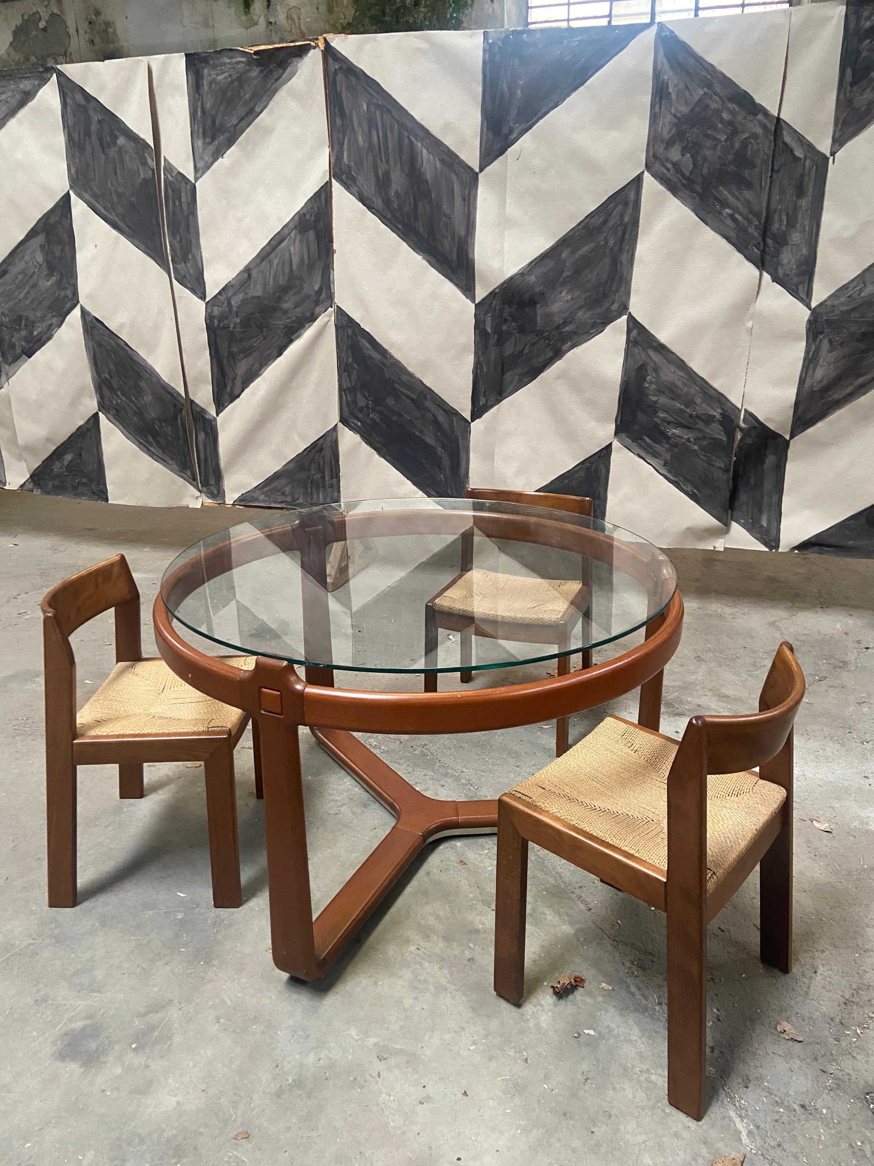 Mid-Century Modern Italian round cherry wood table with smoked glass top and 3 wooden chairs in the style of Ceccotti. 1970s
The table has an amazing tripod basement and the table top rests on the extension of the legs so that it appears to be