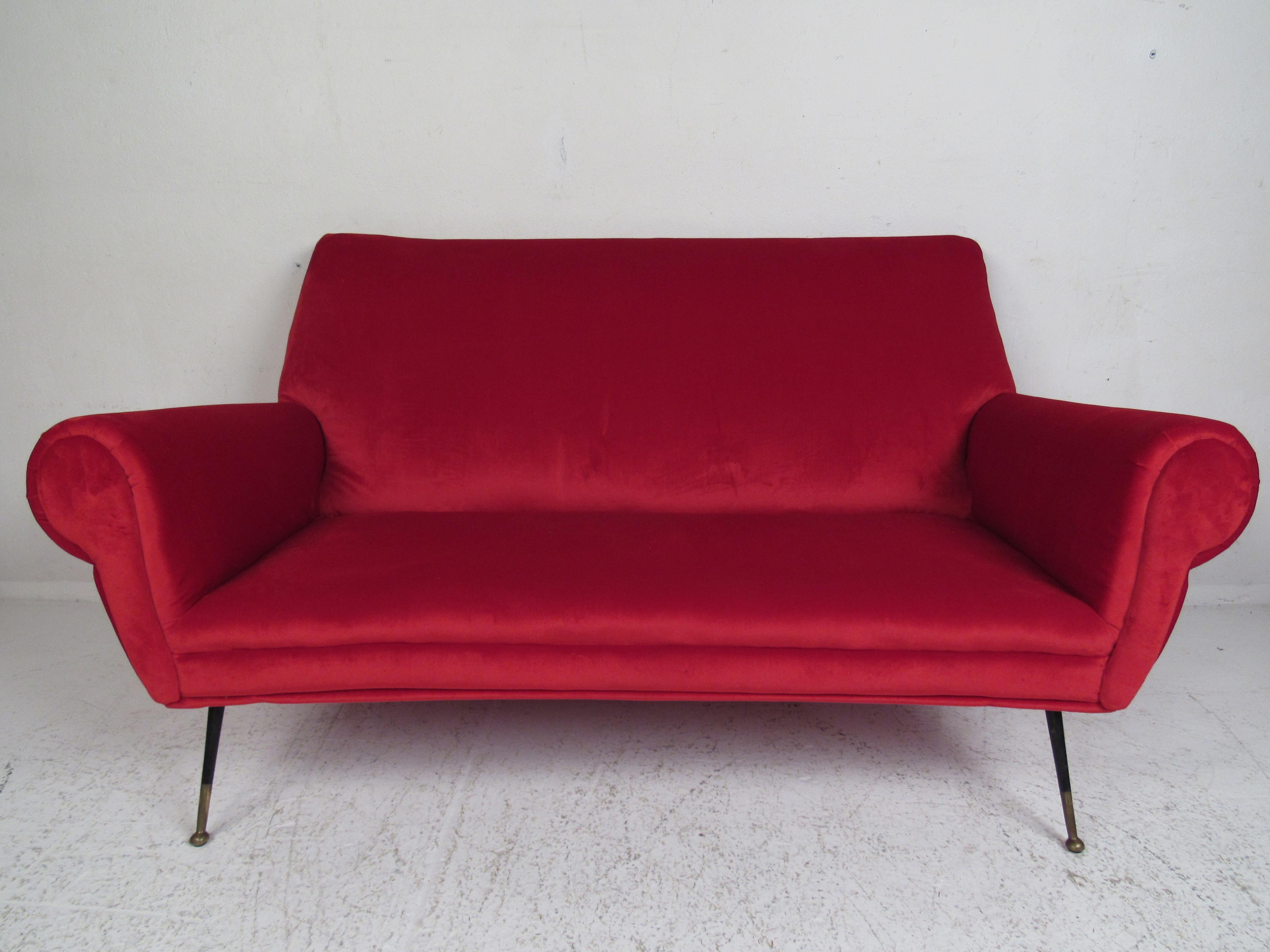This stunning vintage modern Italian settee features ruby red velvet fabric and splayed metal legs with brass feet. The plush upholstery and thick padded seating ensure maximum comfort in any modern interior. Please confirm item location (NY or NJ).