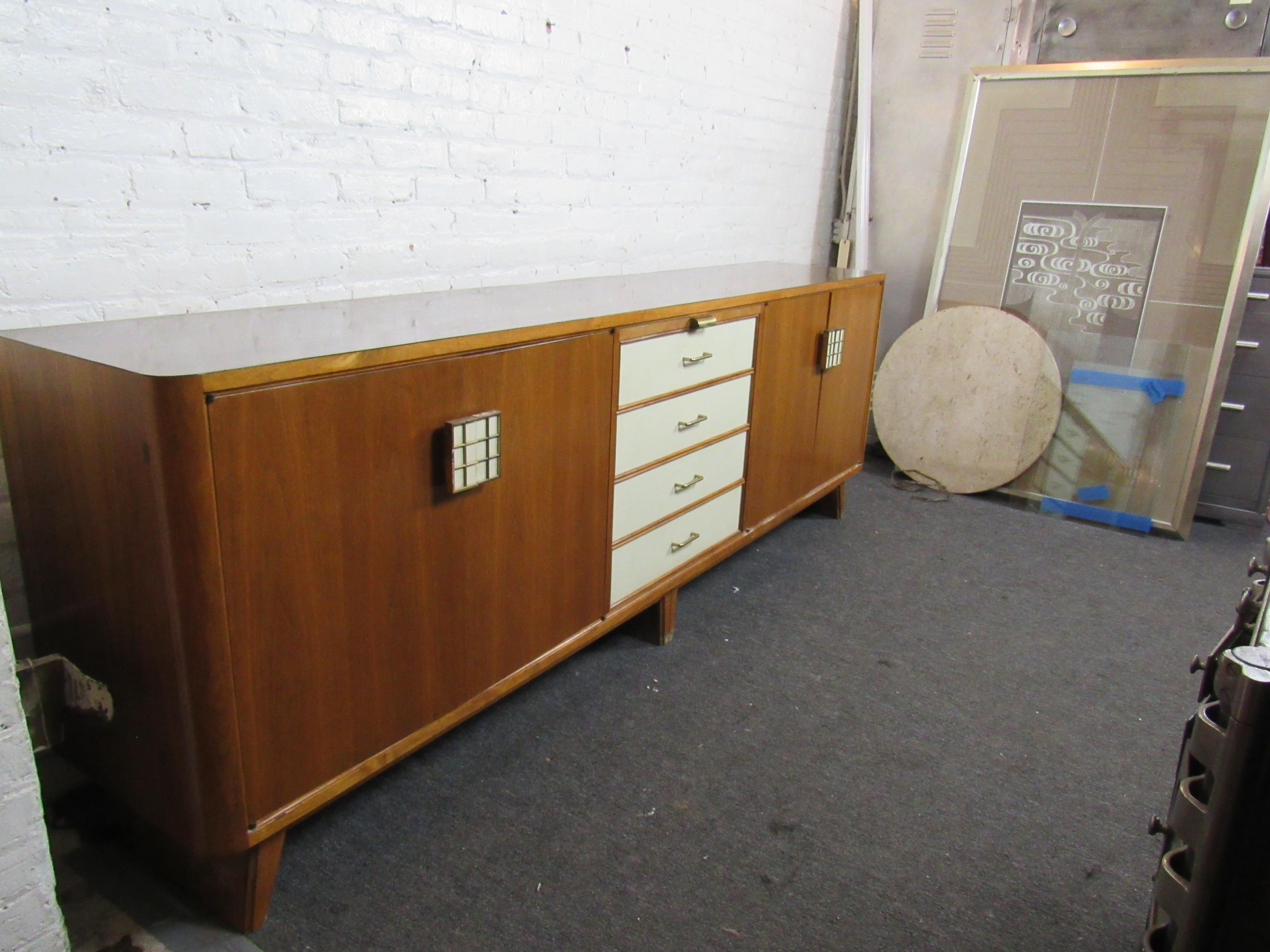 Large Mid-Century Modern, walnut credenza. With an Italian style, this piece features four white drawers in the middle and two cabinets on the side. Both cabinets have four open drawers that slide out. Unique white and brass handles on cabinets.