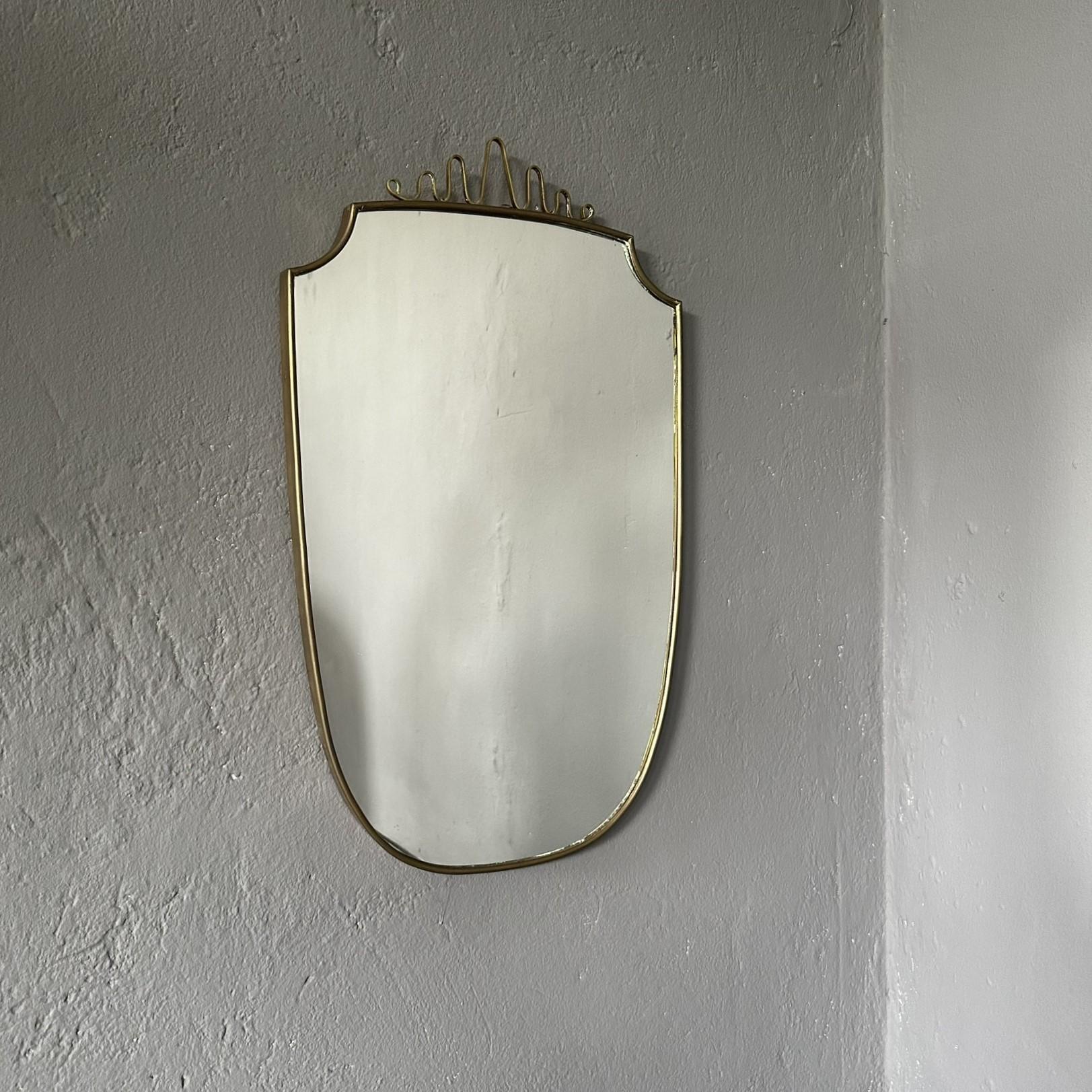 Mid-Century Modern Italian wall mirror, 1950, with brass frame and decoration.

1950s wall mirror, Italian manufacture, made in the style of Giò Ponti.
The mirror has a brass frame with decoration on the top.
Overall height 87cm.
On the decoration,
