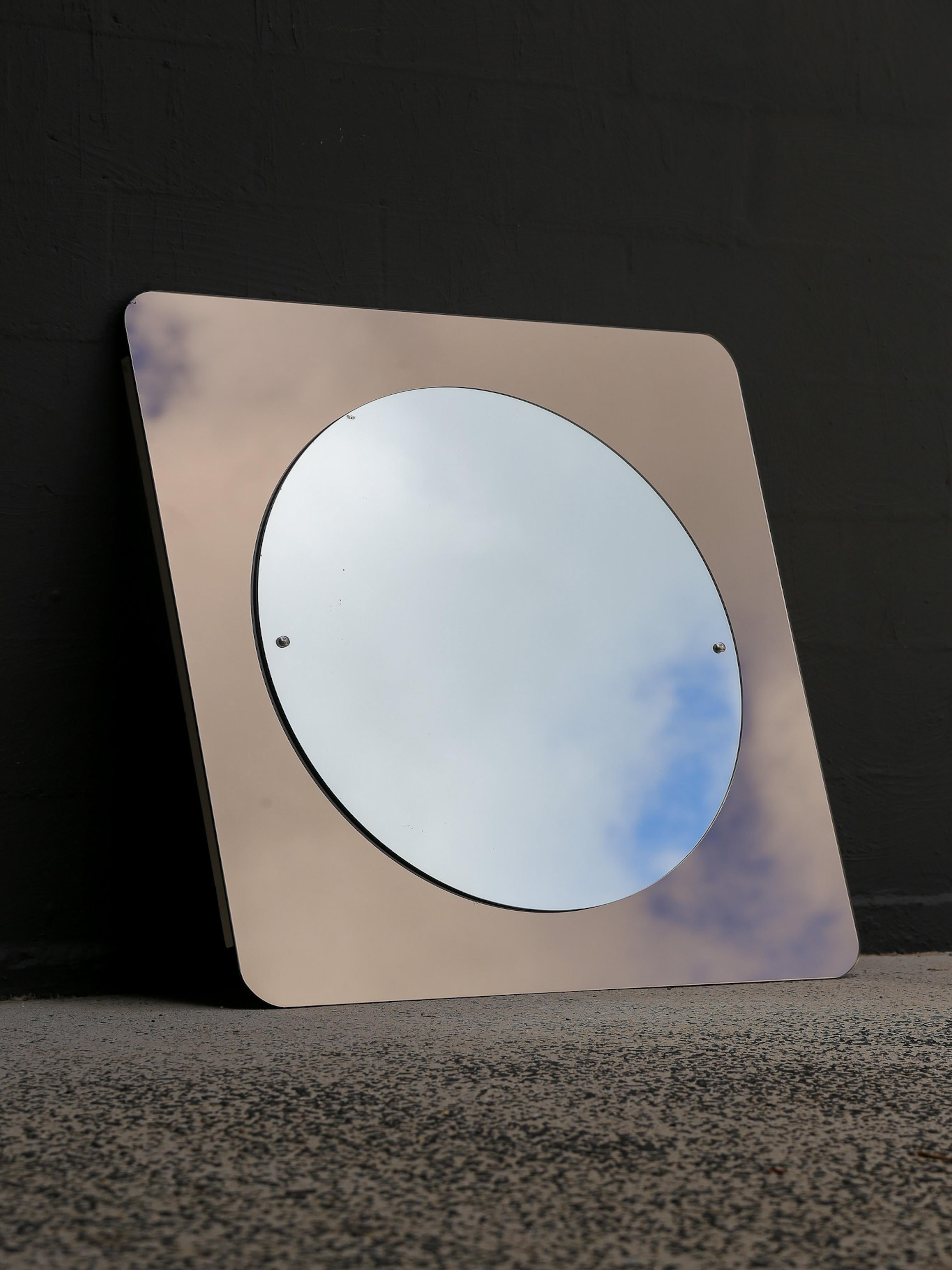 Exemple étonnant du design italien des années 1970, ce miroir mural présente une esthétique géométrique distinctive. Le cadre carré, fabriqué en verre teinté, contraste élégamment avec le miroir central circulaire, créant un effet visuel saisissant.
