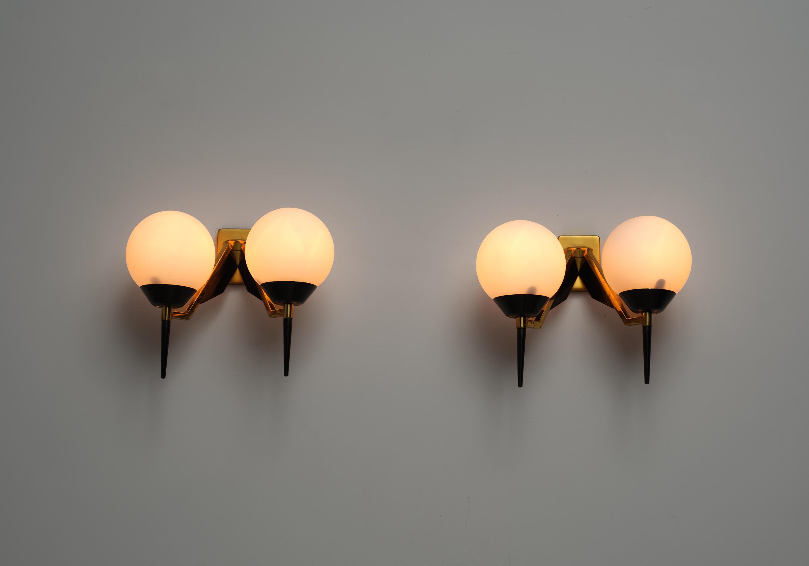 This pair of wall sconces exemplifies elegant and refined Italian design from the 1950s, attributed to Stilnovo. Crafted from high-quality materials, each sconce features a structure of polished brass and black lacquered steel. The design includes
