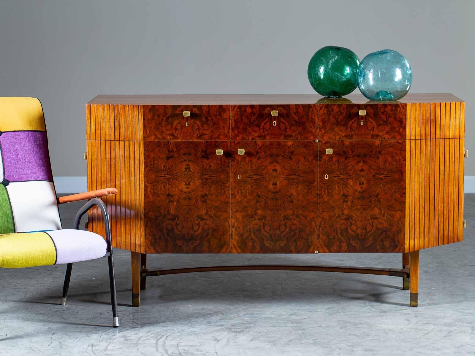 A striking Mid-Century Modern Italian burl walnut buffet credenza circa 1950 featuring the original brass hardware. This unique Italian cabinet has a surprising façade with a straight front flanked by front sides that slant toward the back. Designed