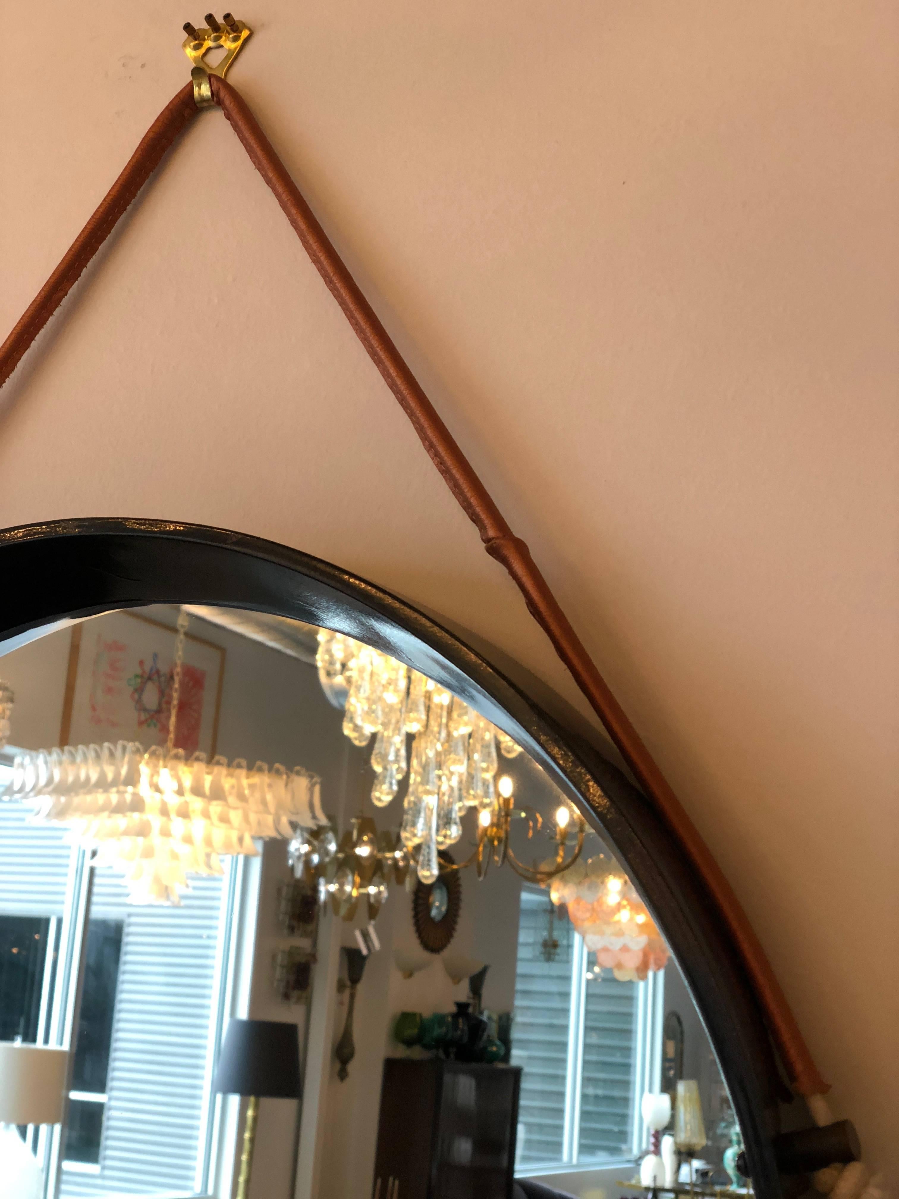 Offered is a mid century modern Jacques Adnet style newly lacquered in black and new leather strap in metallic copper hanging wall mirror. This modern mirror is a true testament to Mid-Century Modern design. This simple yet strong statement piece