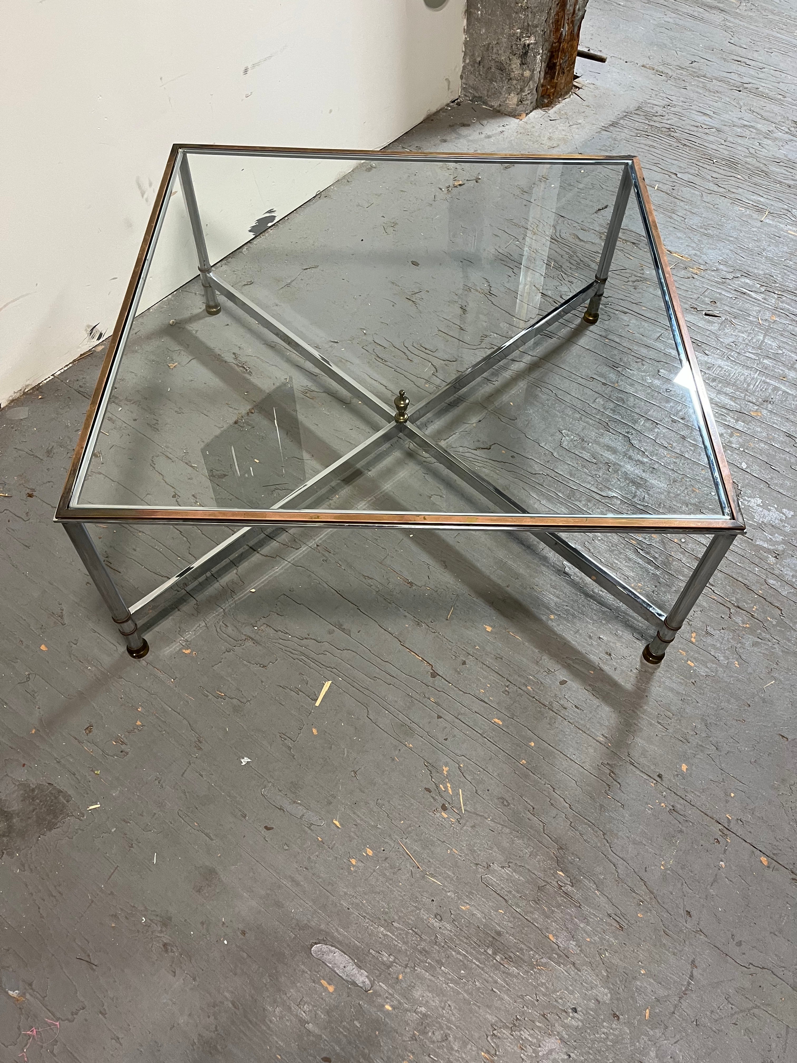 Table basse en chrome et laiton du milieu du 20e siècle avec plateau en verre. Dans le style de la Maison Jansen. Laiton patiné riche et profond. Joliment détaillé avec des bandes en laiton autour des pieds, une lèvre en laiton surélevée et un épi