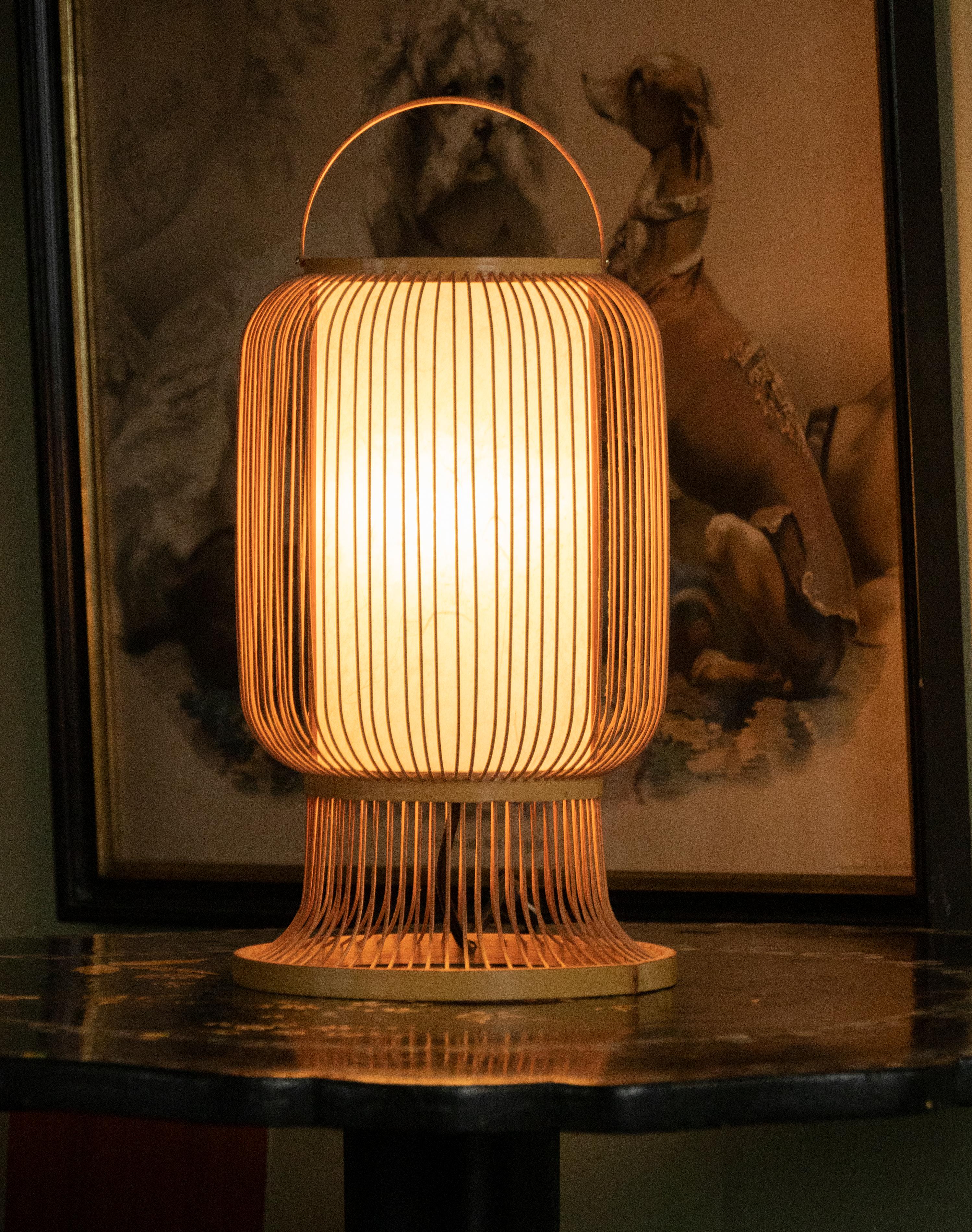 A beautiful Japanese lantern-shaped table lamp. Made of thin bamboo spokes with a cylinder paper shade. Takes one standard size light E27 bulb. It has an organic feel and will provide a beautiful ambient light. With the original switch and plug.