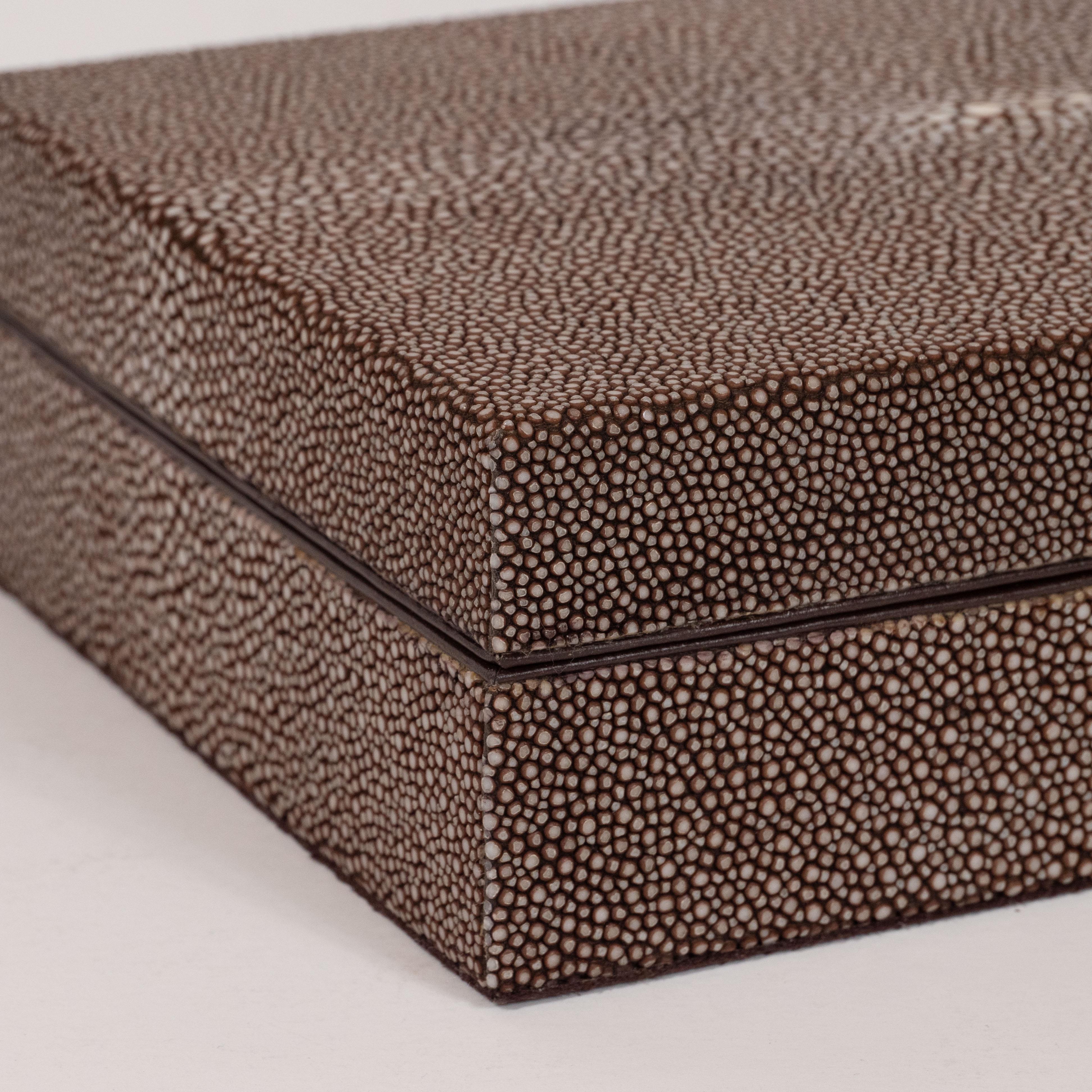 This stunning Mid-Century Modern decorative lidded box offers a volumetric rectangular box covered in java and cream hued shagreen- showcasing the inherent natural grain of the material. The interior of the box is lined in coffee hued suede. While