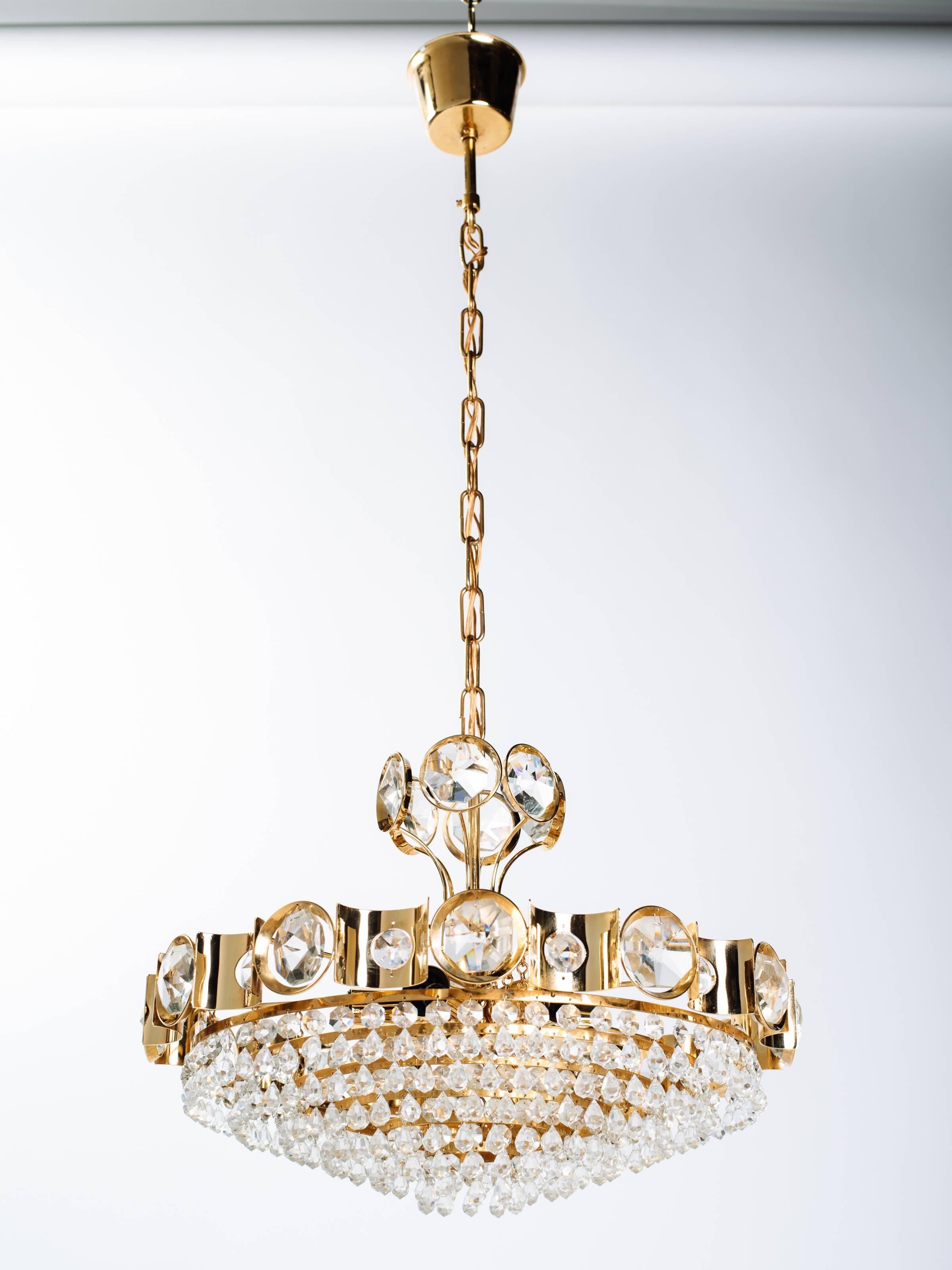 Exquisite Hollywood Regency chandelier with gold-plated over brass frame. The chandelier has a circular multi-tiered design with scalloped details. Fitted with rows of cut crystals and stunning oversized jeweled crystals along the top. Chandelier is