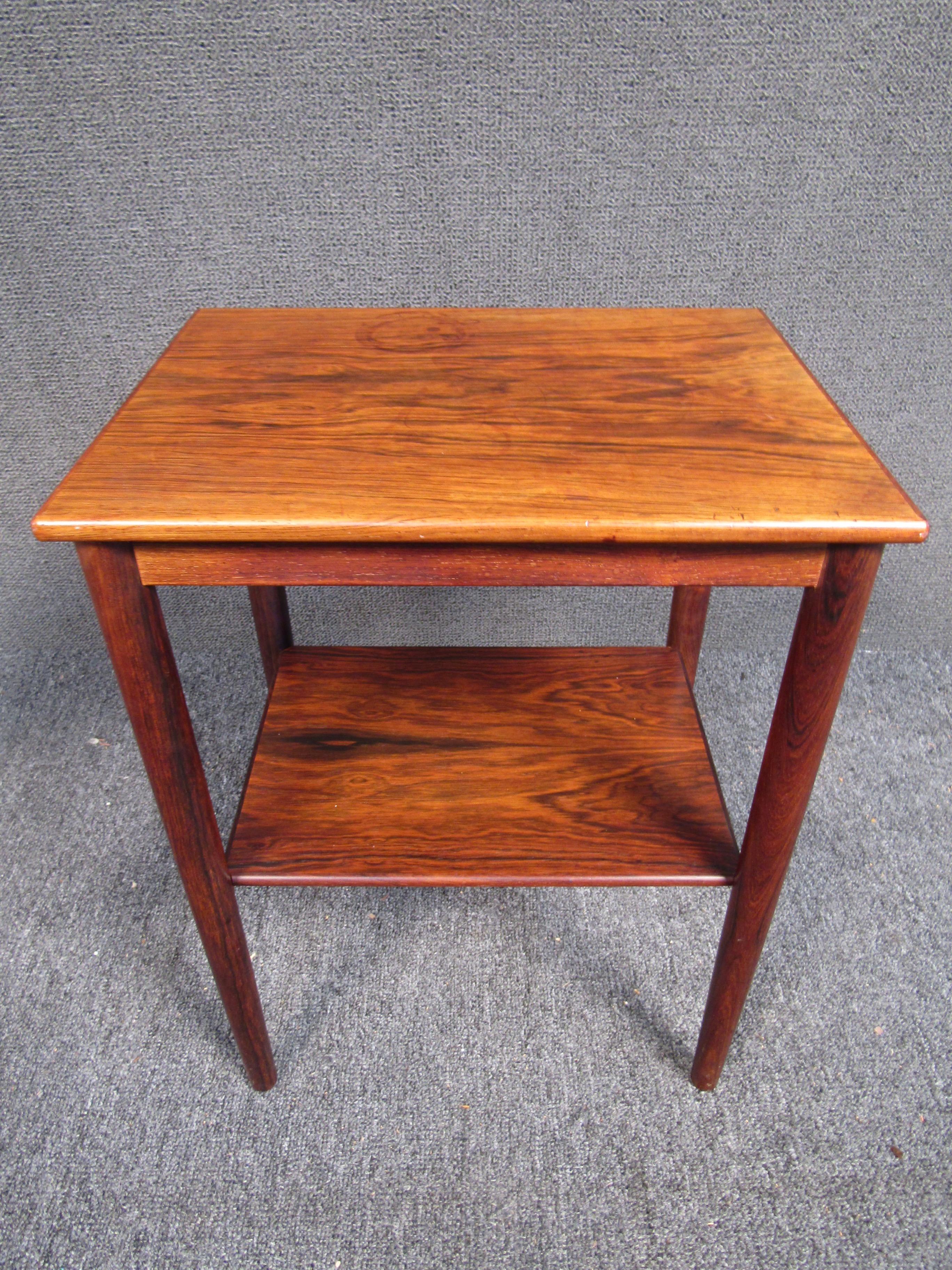 Stunning John Stuart vintage modern end table. The unique two-tier design offers plenty of room for storage with a sleek overhang on top. Gorgeous rosewood grain, rounded edges on the top, and tapered legs add to the allure. This Mid-Century side