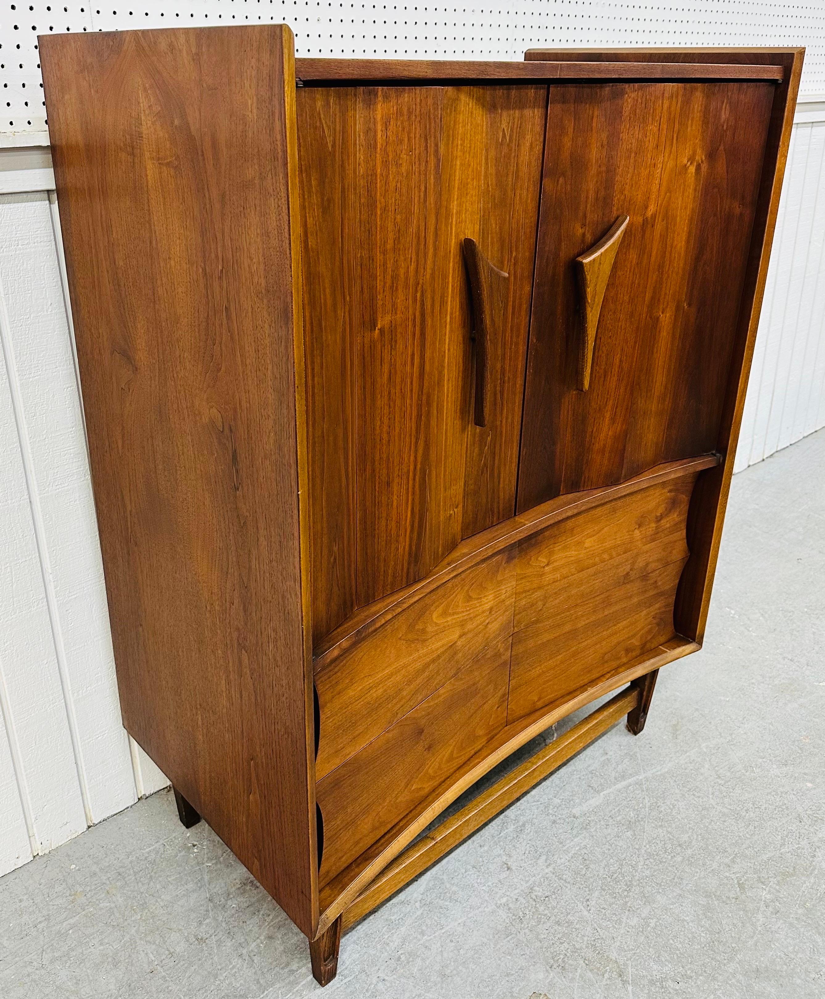 This listing is for a Mid-Century Modern Kagan Style Walnut High Chest. Featuring a straight line design, two doors with sculpted wooden pulls that open up to three hidden drawers, two larger drawers at the bottom, modern legs with a stretcher, and