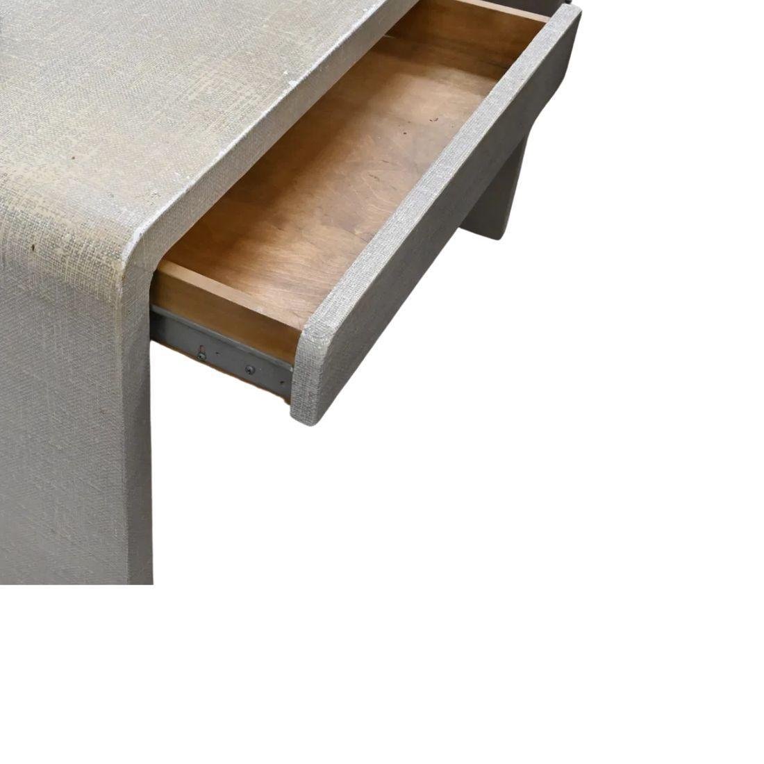 A vintage Mid-Century Modern Karl Springer style console table with two drawers.  The cream colored console table has a waterfall edge to each side and two drawers that seamlessly blend into the table's apron. Stylish and functional as a desk or