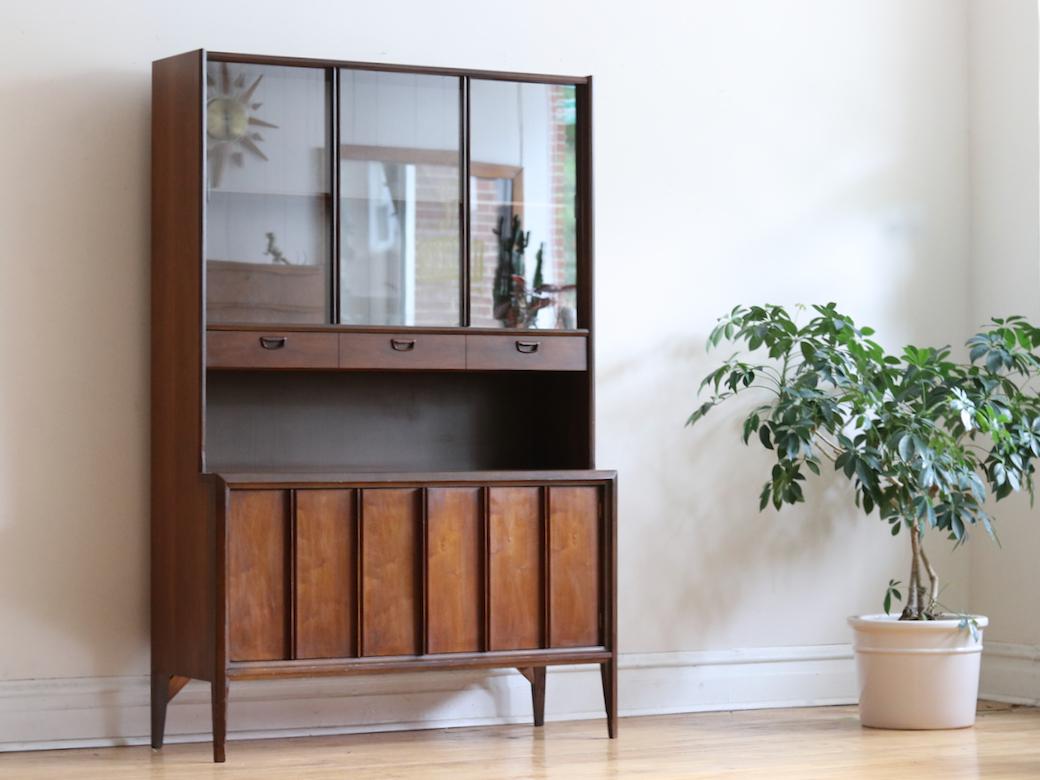 Mid-Century Modern walnut china cabinet made by Keller Furniture.
Sliding glass panels on top display case.
One long divided dovetailed drawer.
Walnut with laminate counter top. 
Enclosed storage space below.
Single piece unit.
Excellent