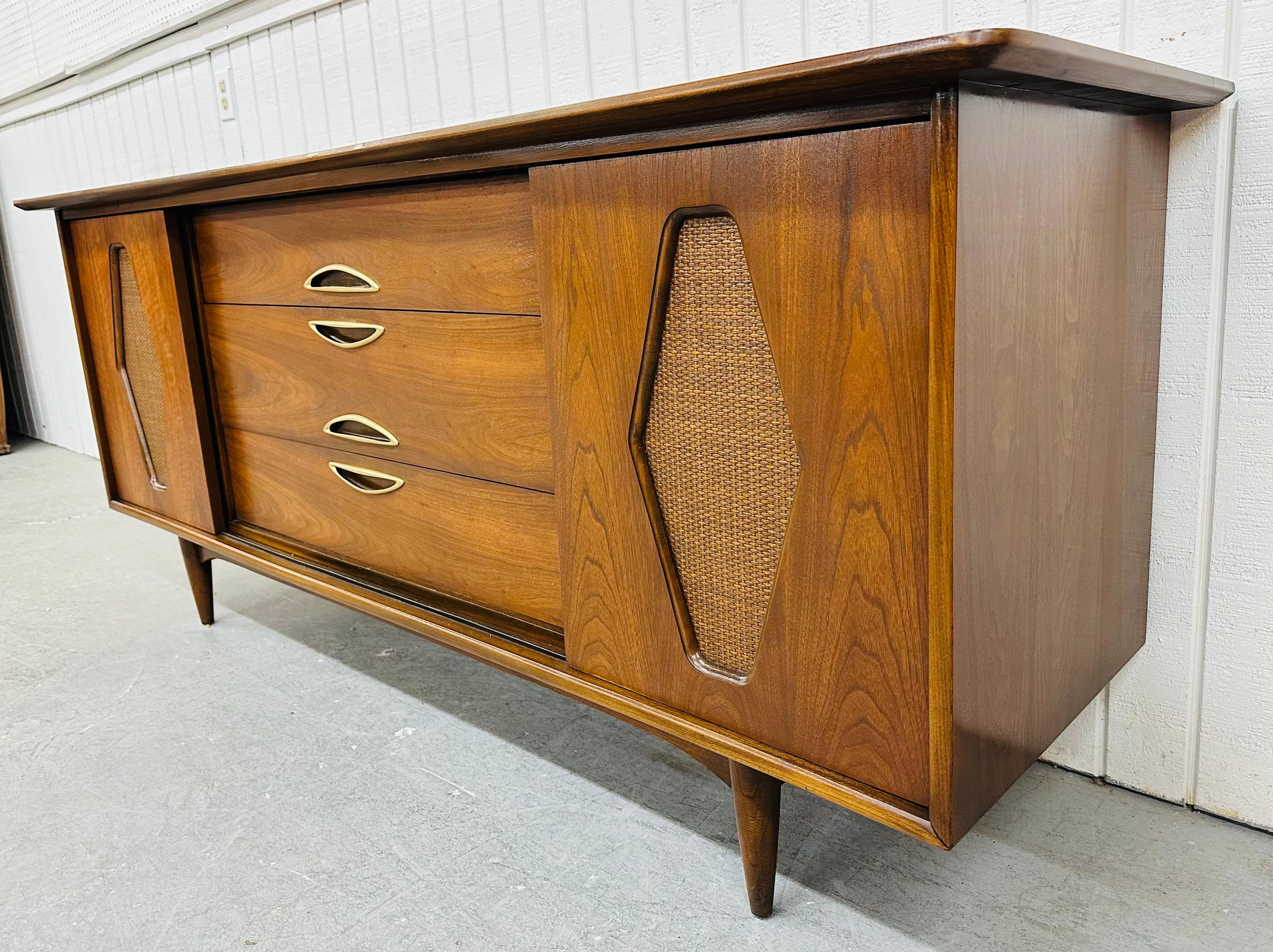 This listing is for a Mid-Century Modern Kent Coffey Greenbrier Walnut Dresser. Featuring a unique shaped top, sliding cane doors that reveal six hidden drawers, three larger drawers in the center, original brass hardware, modern legs, and a