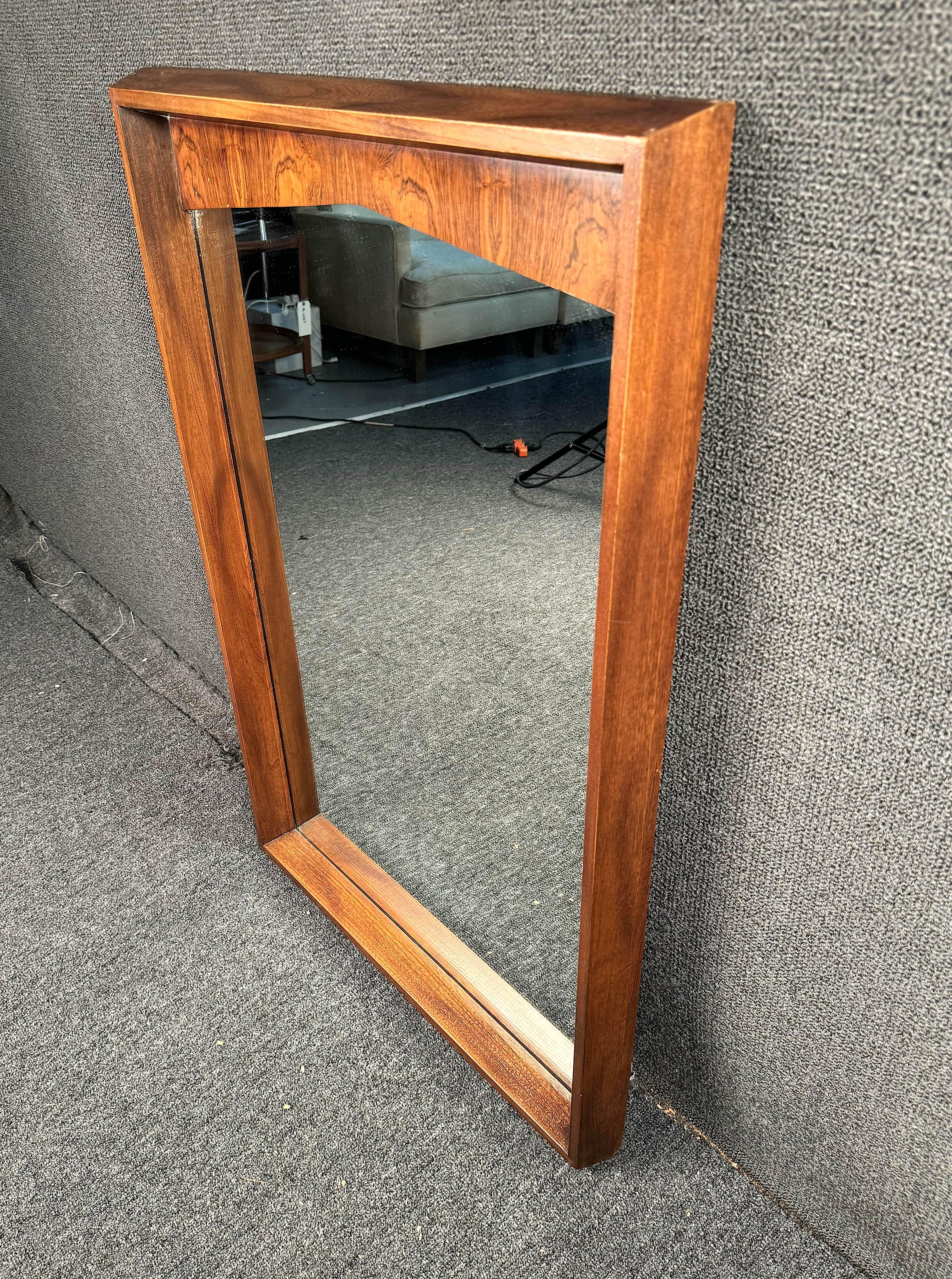 Mid-Century Modern Kent Coffey Wandspiegel. Er hat ein geradliniges, rechteckiges Design mit geschwungener Oberseite, einen Massivholzrahmen, einen abgeschrägten Spiegel und einen Rosenholzakzent an der Oberseite. Dies ist eine außergewöhnliche