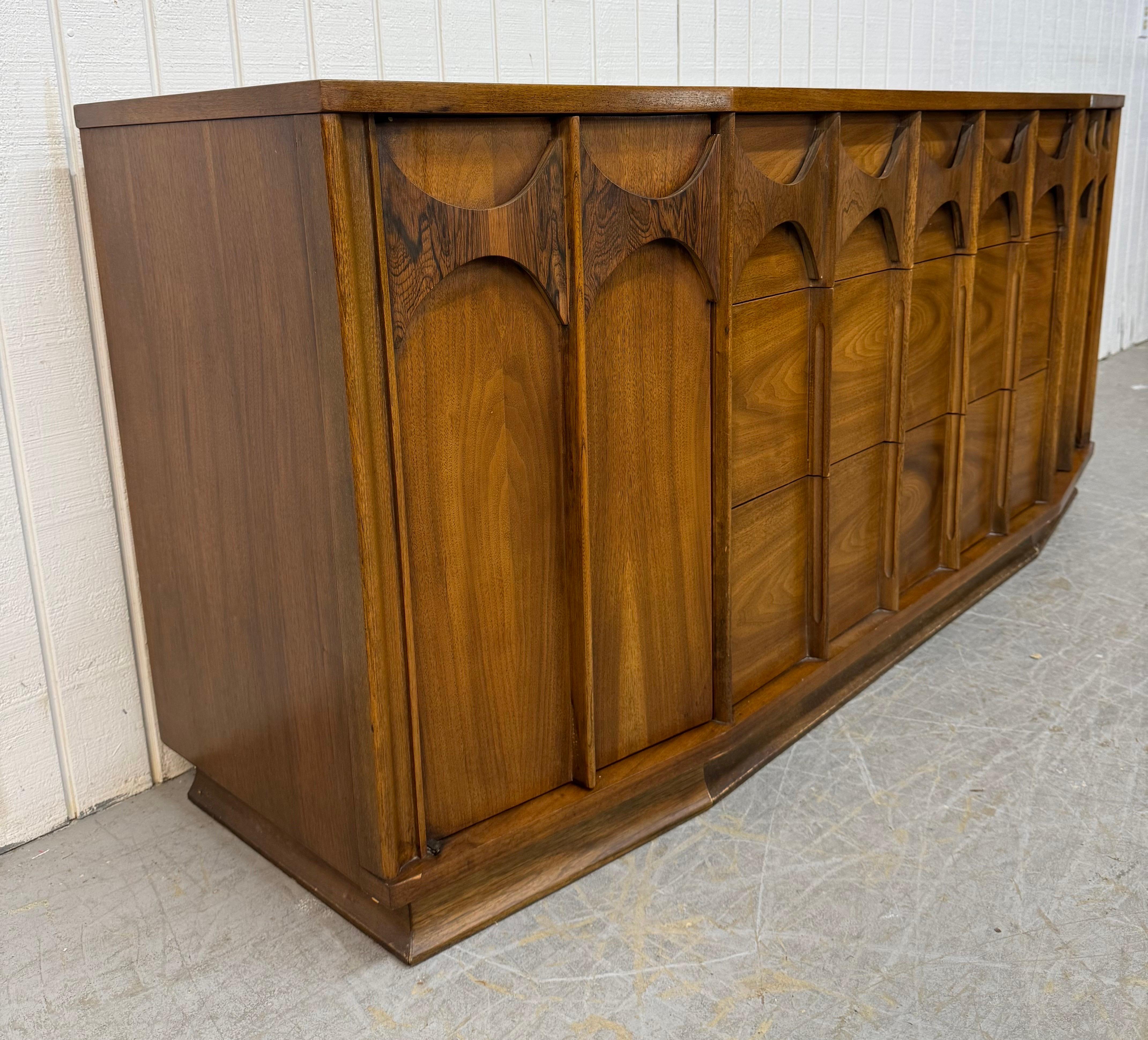 Questo annuncio si riferisce a un comò a 9 cassetti in noce Kent Coffey Perspecta. Caratterizzato da un design lineare, due ante su ogni estremità che si aprono su cassetti nascosti, tre grandi cassetti al centro, tiretti in legno scolpiti, base a