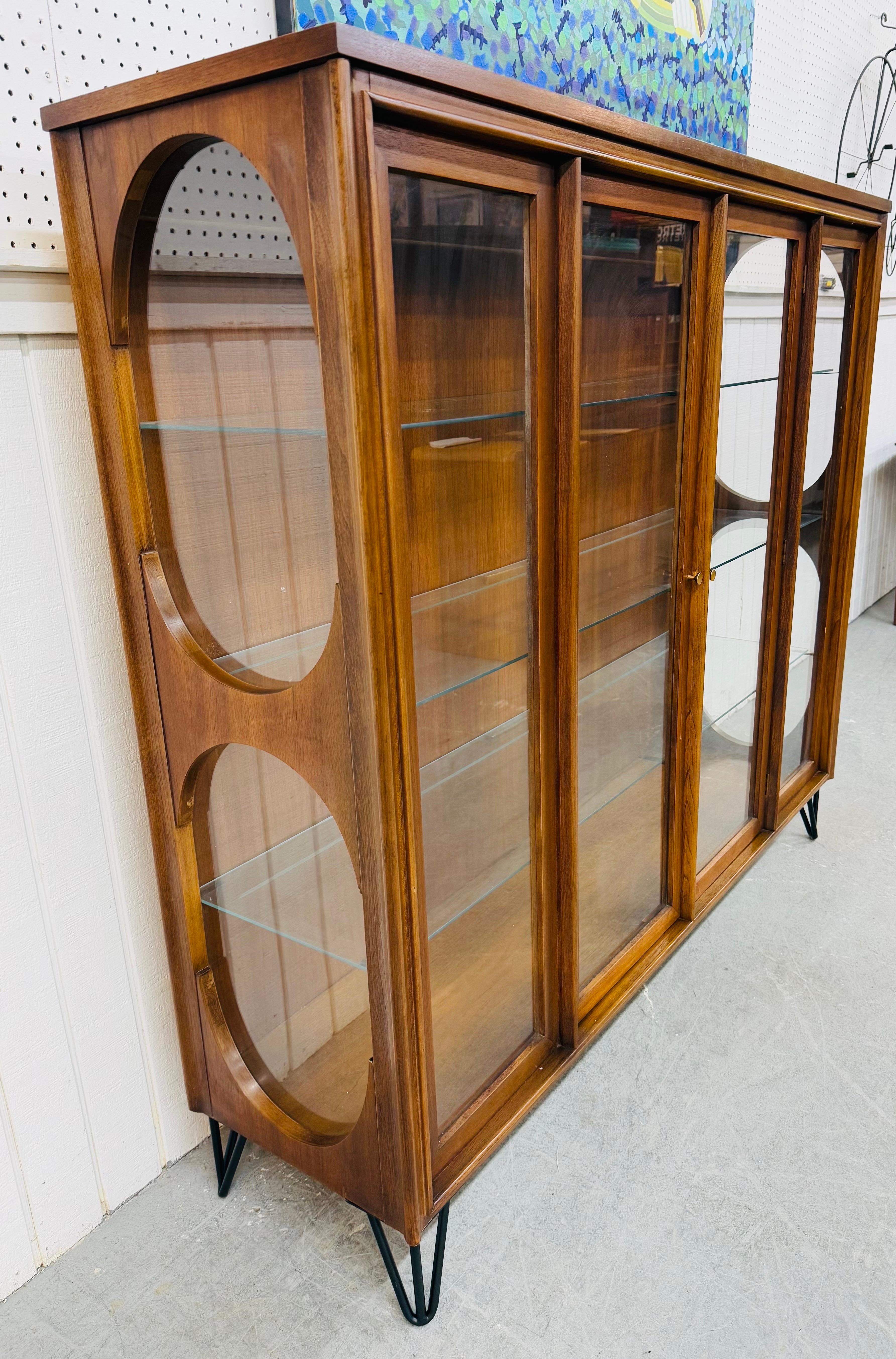 This listing is for a Mid-Century Modern Kent Coffey Perspecta Walnut Display Cabinet. Featuring a straight line design, two doors that open up to three glass shelves, oval glass side panels, black hairpin legs, and a beautiful walnut finish. This
