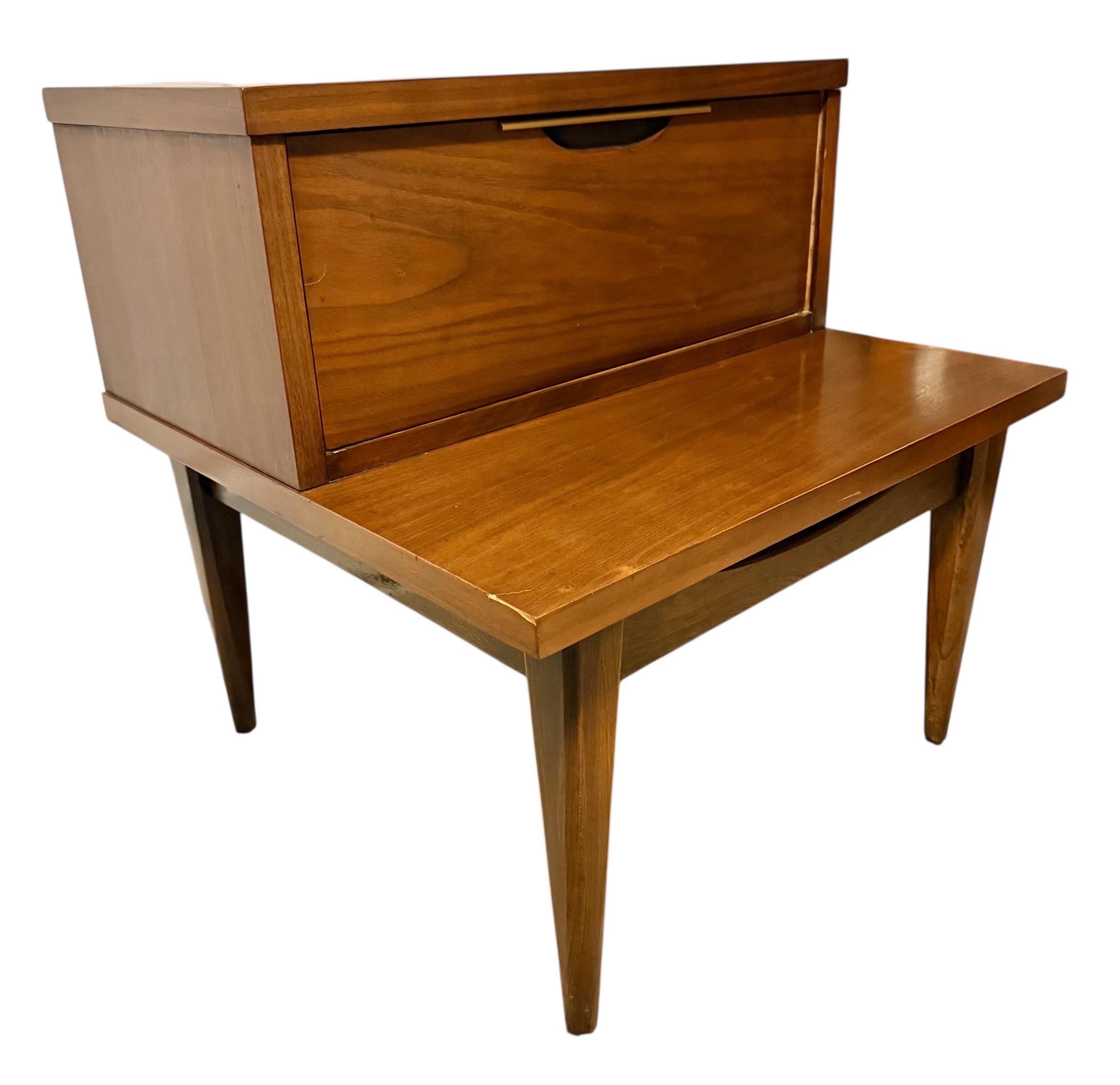 This listing is for a single Mid-Century Modern Kent Coffey Tableau Walnut Nightstand. Featuring a straight line step design, single drawer with recessed brass pull, long modern legs, and an original walnut finish. This is an exceptional combination