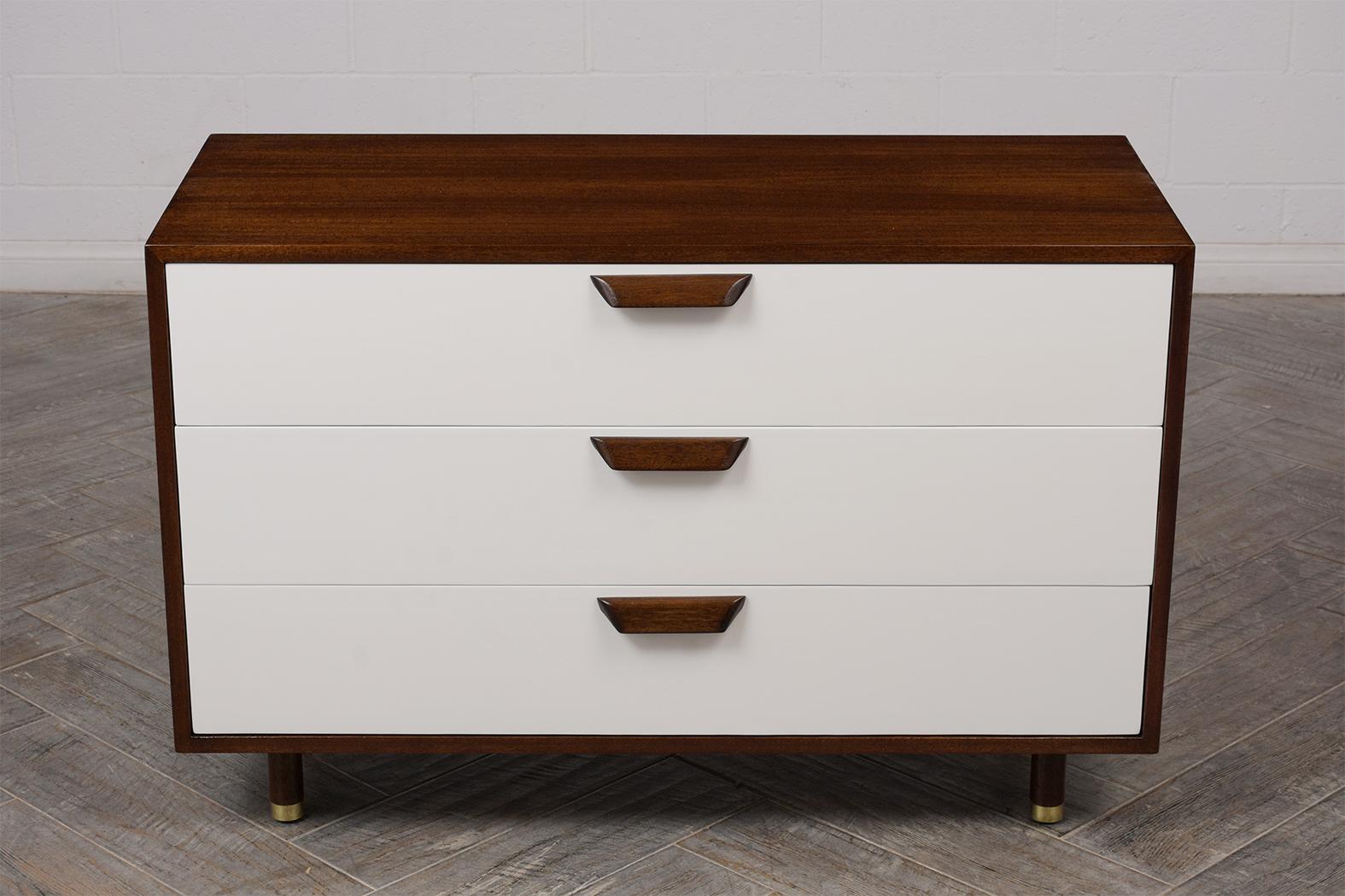 This completely restored midcentury style chest of drawers is stained in a dark walnut and white color combination with a lacquered finish. It features 3 large white drawers with walnut pulls. The chest is raised on four tapered pedestal legs with