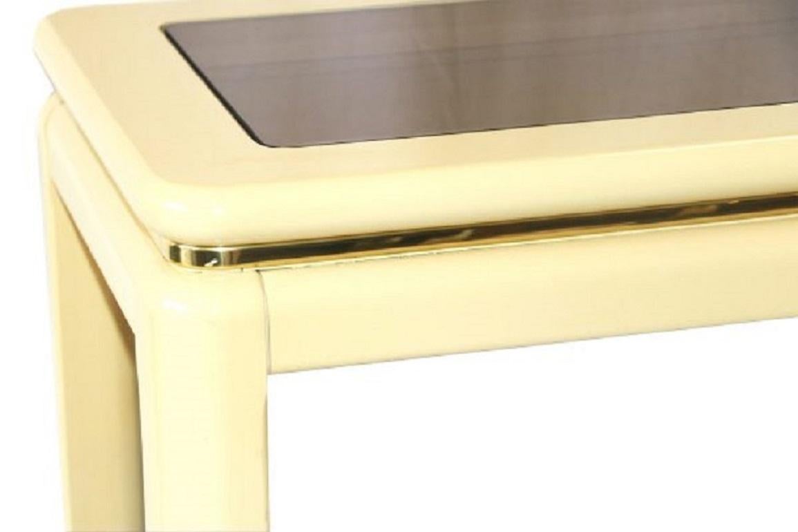 A lovely mid-century lacquer finished console table with smoke glass insert by Lane Furniture. The

table displays a high gloss ivory / cream finish with smooth, rounded edges on the entire piece. The top

has an inlay of smoked glass and flows