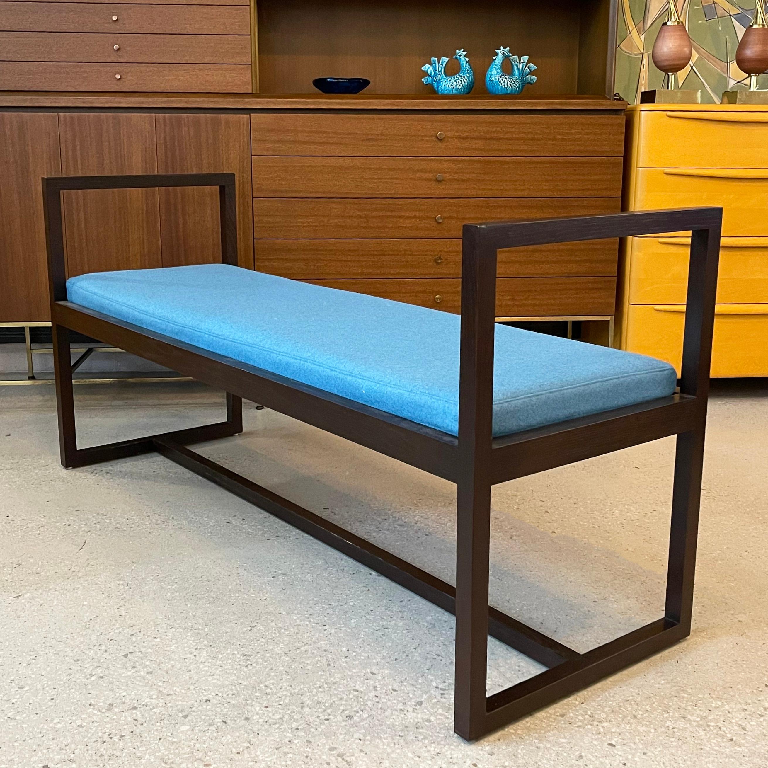 Mid-century modern bench features a clean, geometric, lacquered mahogany frame with high handled sides and contrasting bright blue wool upholstered seat. It's perfect as accent seating or entryway bench.