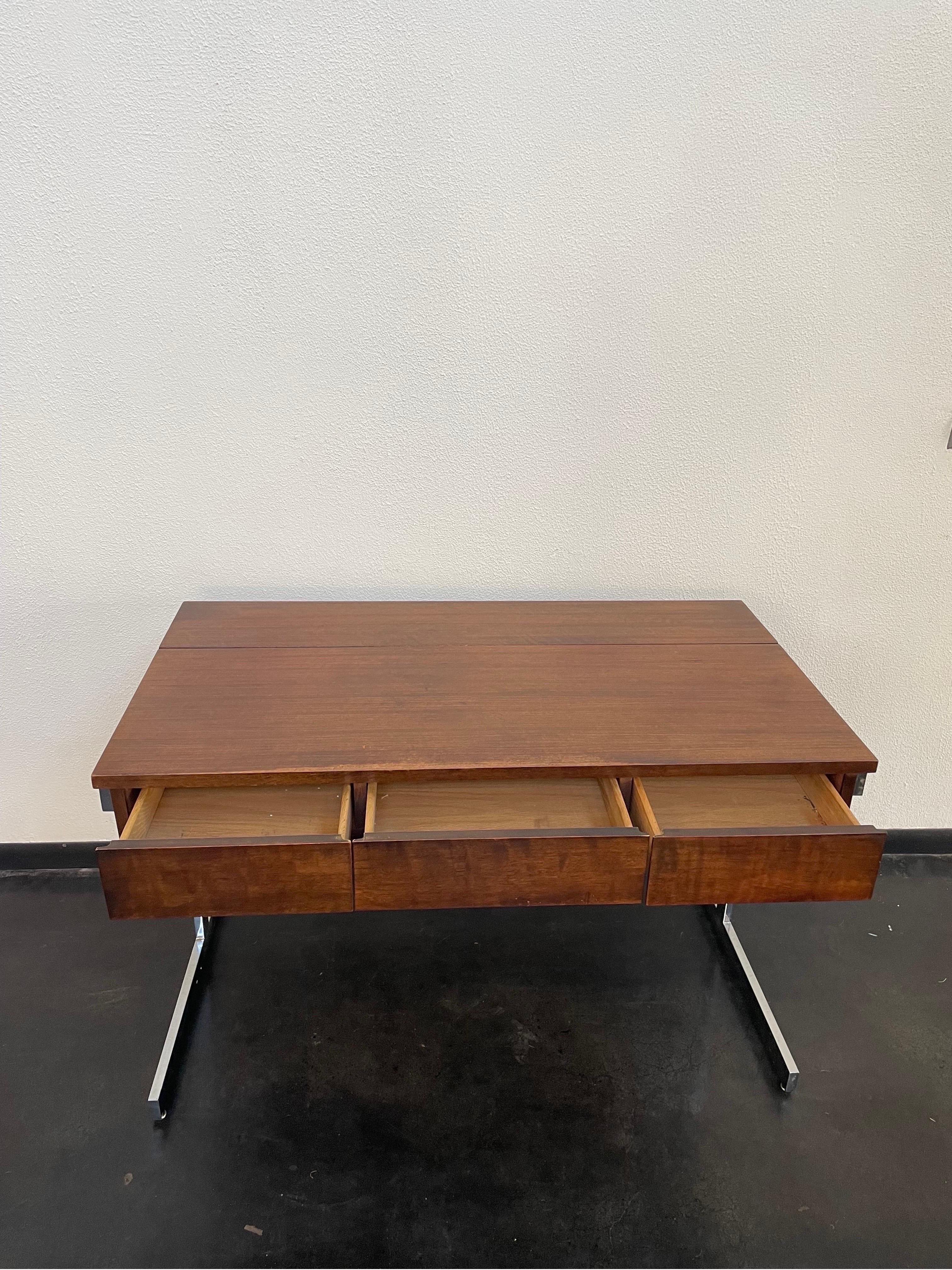 Solid rosewood Mid-Century Modern desk by Lane Furniture. There are three front side-by-side pullout drawers and a flush lift-top compartment at the back for storage. The desk is finished with T-shaped chrome legs.