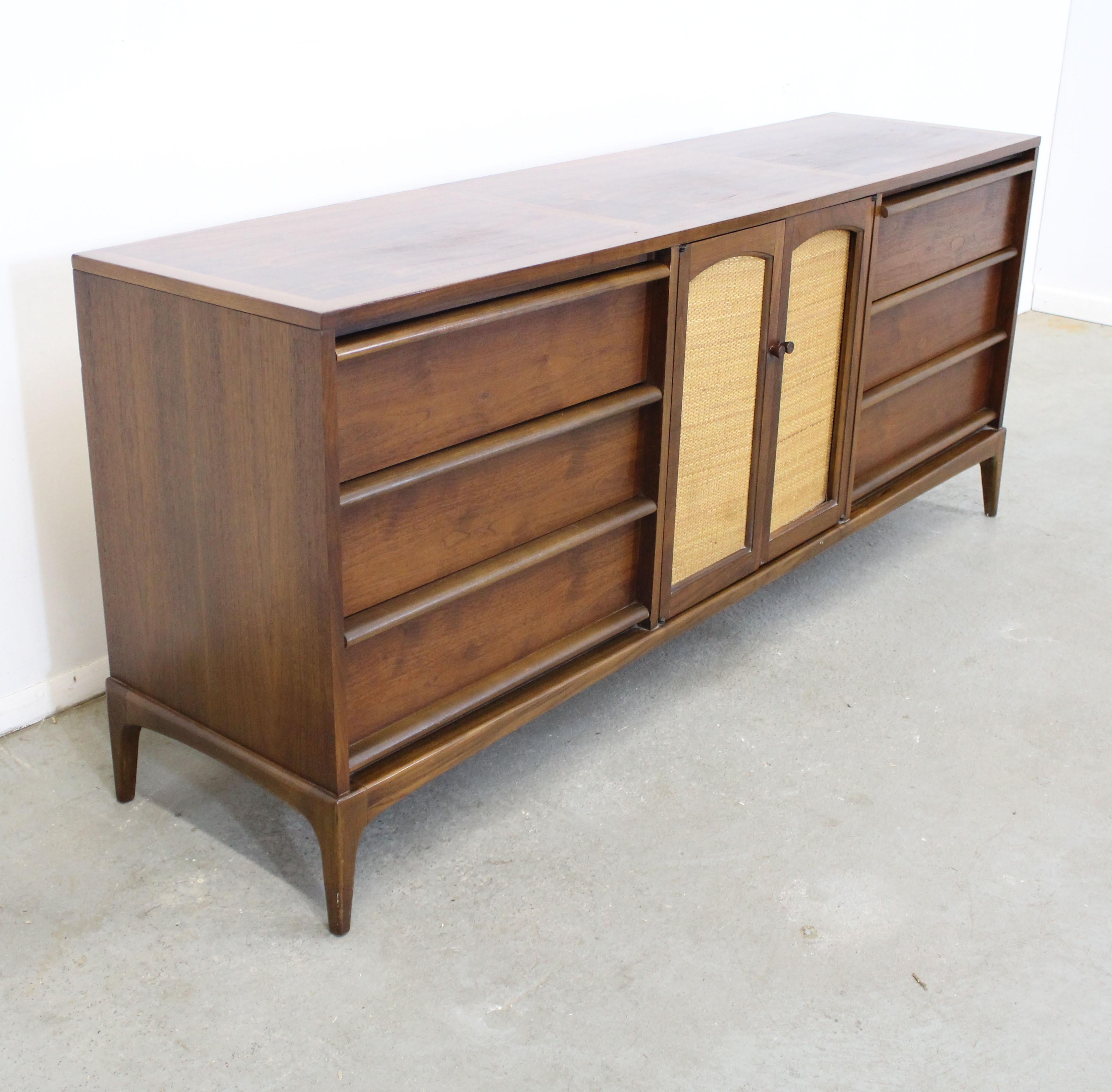 Offered is vintage Mid-Century Modern walnut dresser/credenza by Lane 'Rhythm', circa 1960. This beauty features a beautiful walnut grain, parqueted top, and two centered cane doors with three hidden drawers and 6 side drawers. The doors are